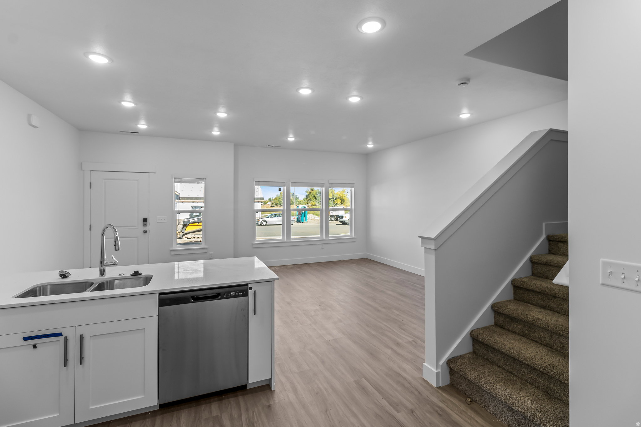 Modern kitchen island featuring a stainless steel double sink with a gooseneck faucet, white cabinetry with contemporary hardware, and a built-in stainless steel dishwasher