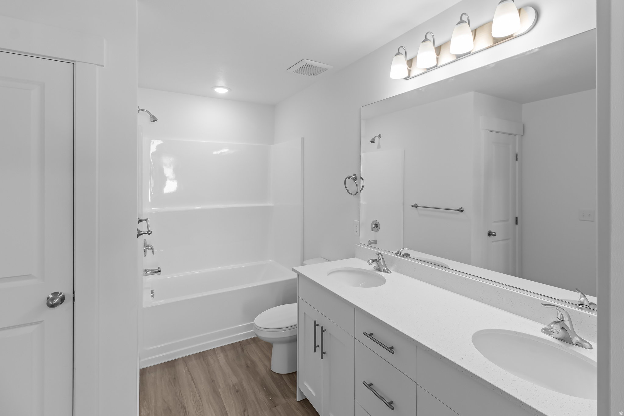 Bathroom featuring a double vanity with white cabinetry and integrated sinks, a full-width mirror, and a white tub/shower combination with chrome fixtures