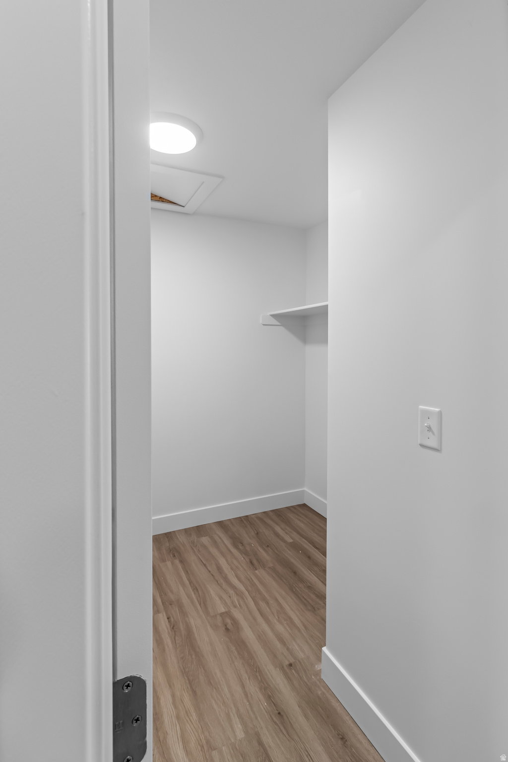 Compact walk-in closet featuring wood-finish flooring, a built-in storage shelf, recessed ceiling lighting, and white baseboards