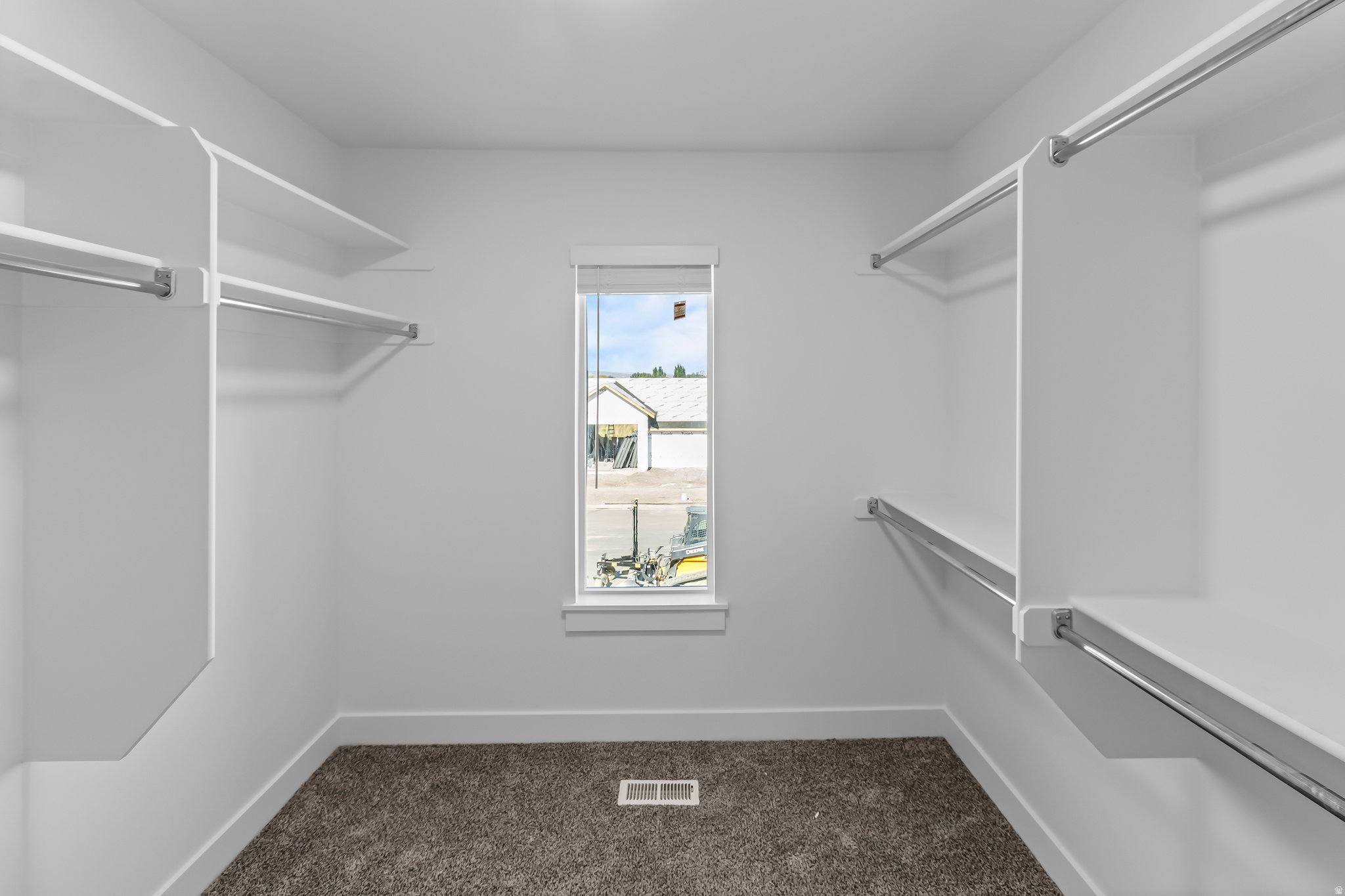 Walk-in closet featuring built-in shelving, chrome hanging rods, a single window with white trim, and dark textured carpeting