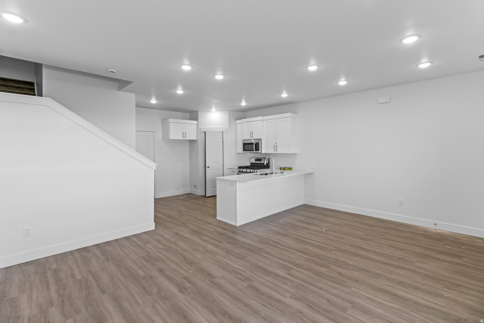 Open-concept living area featuring wood-finish flooring, recessed lighting, and a kitchen with white cabinetry and stainless steel appliances