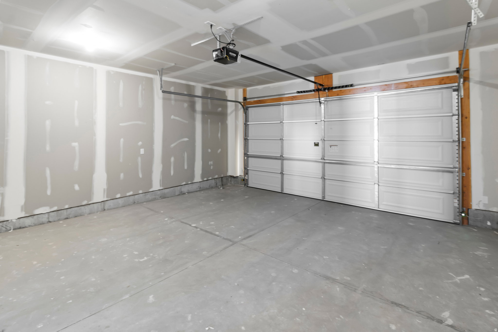 Spacious garage with a sectional garage door, exposed wood framing, and a concrete floor