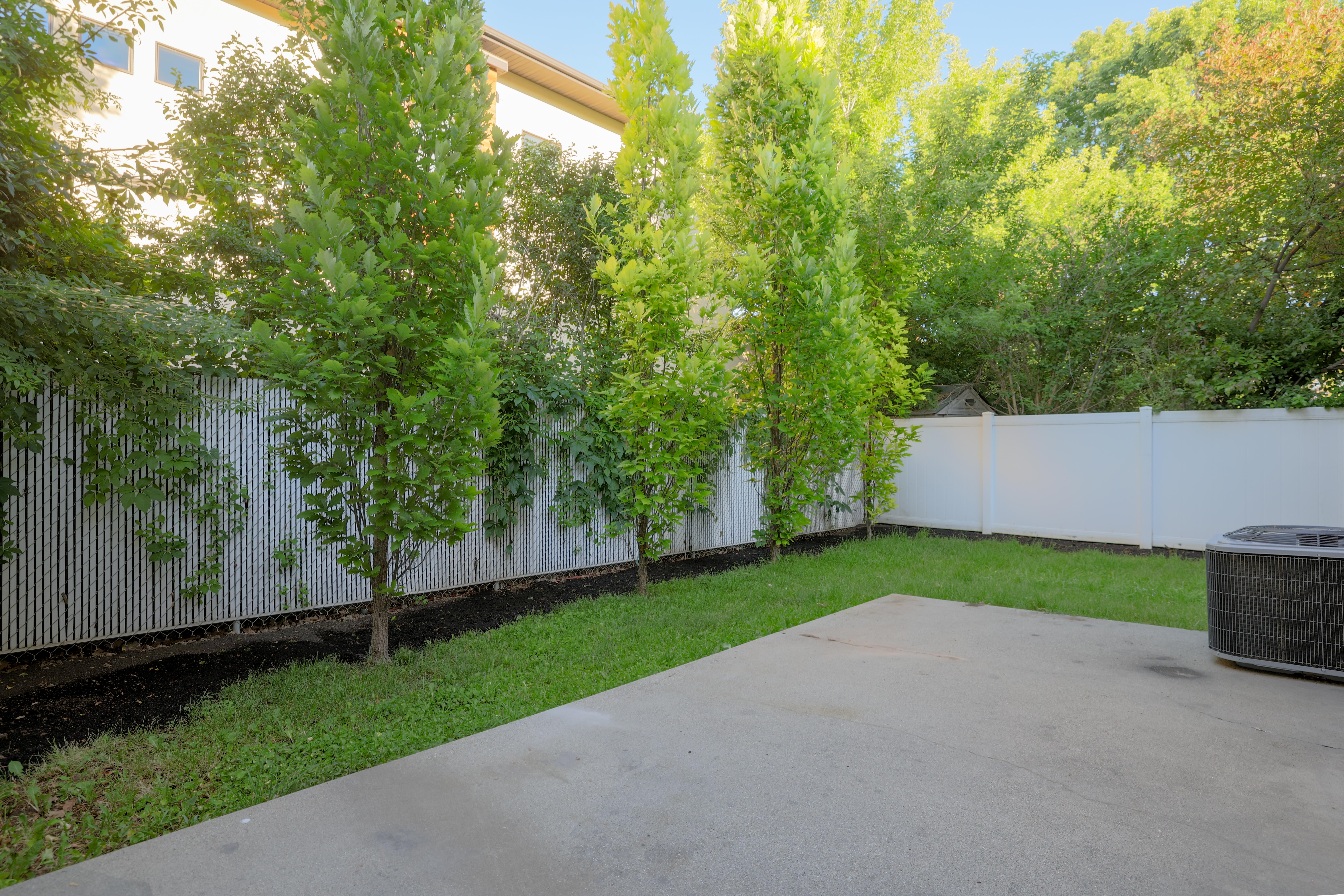 Private backyard featuring a concrete patio, manicured lawn, and mature trees
