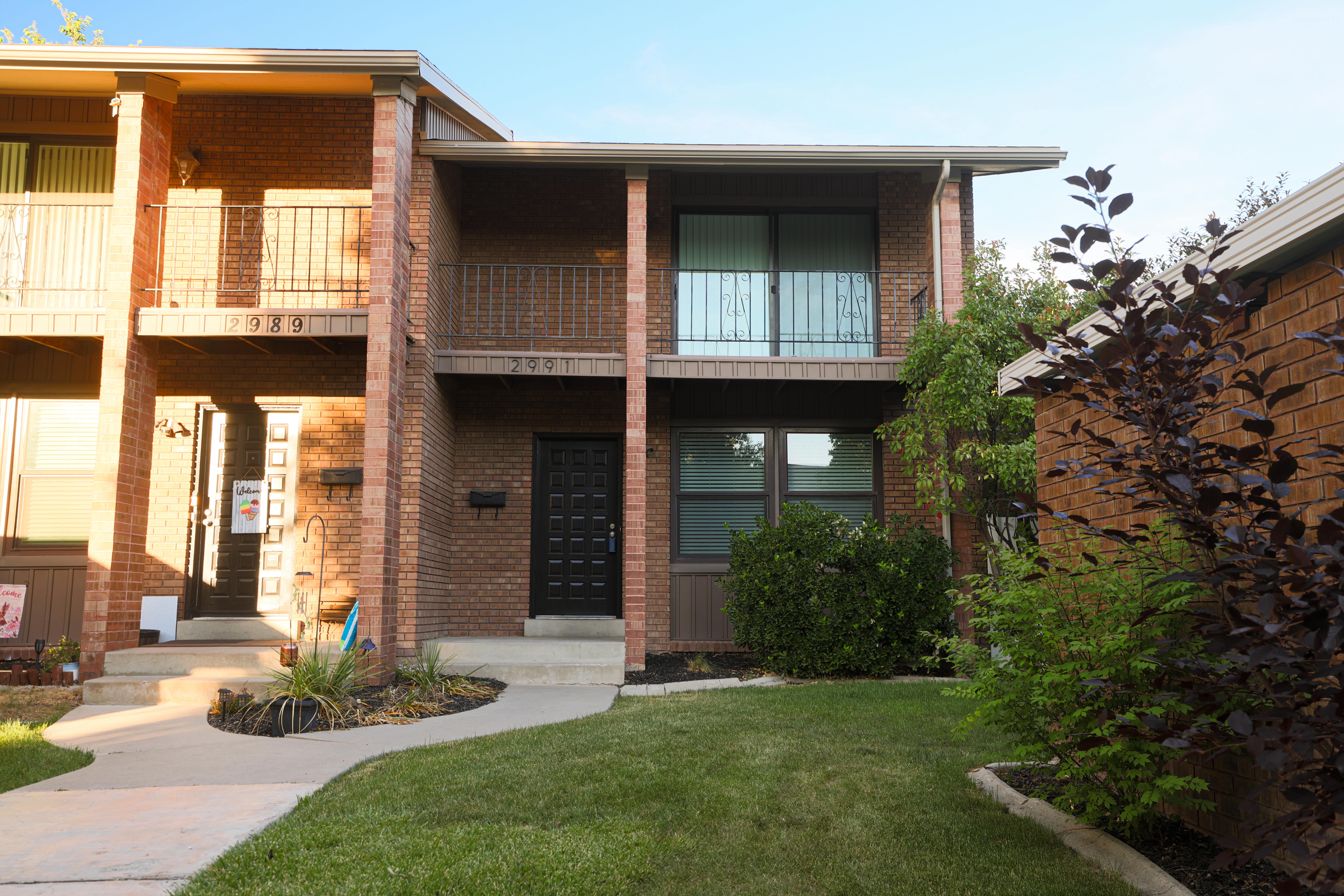 Brick exterior featuring a black front door, a second-story balcony with metal railings, and a well-maintained lawn