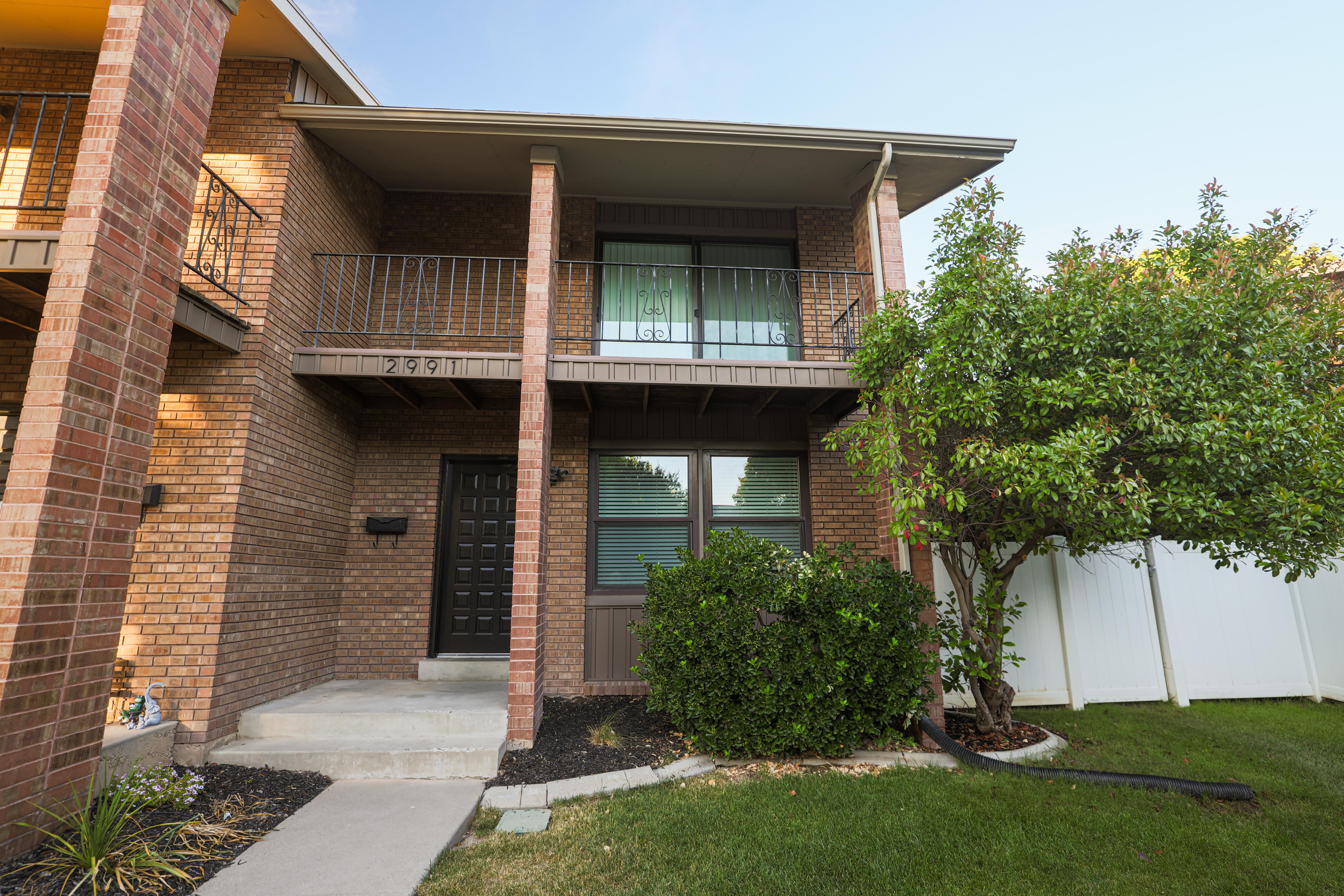 Brick exterior featuring a private balcony with wrought iron railing, concrete entry porch, and ground-level windows