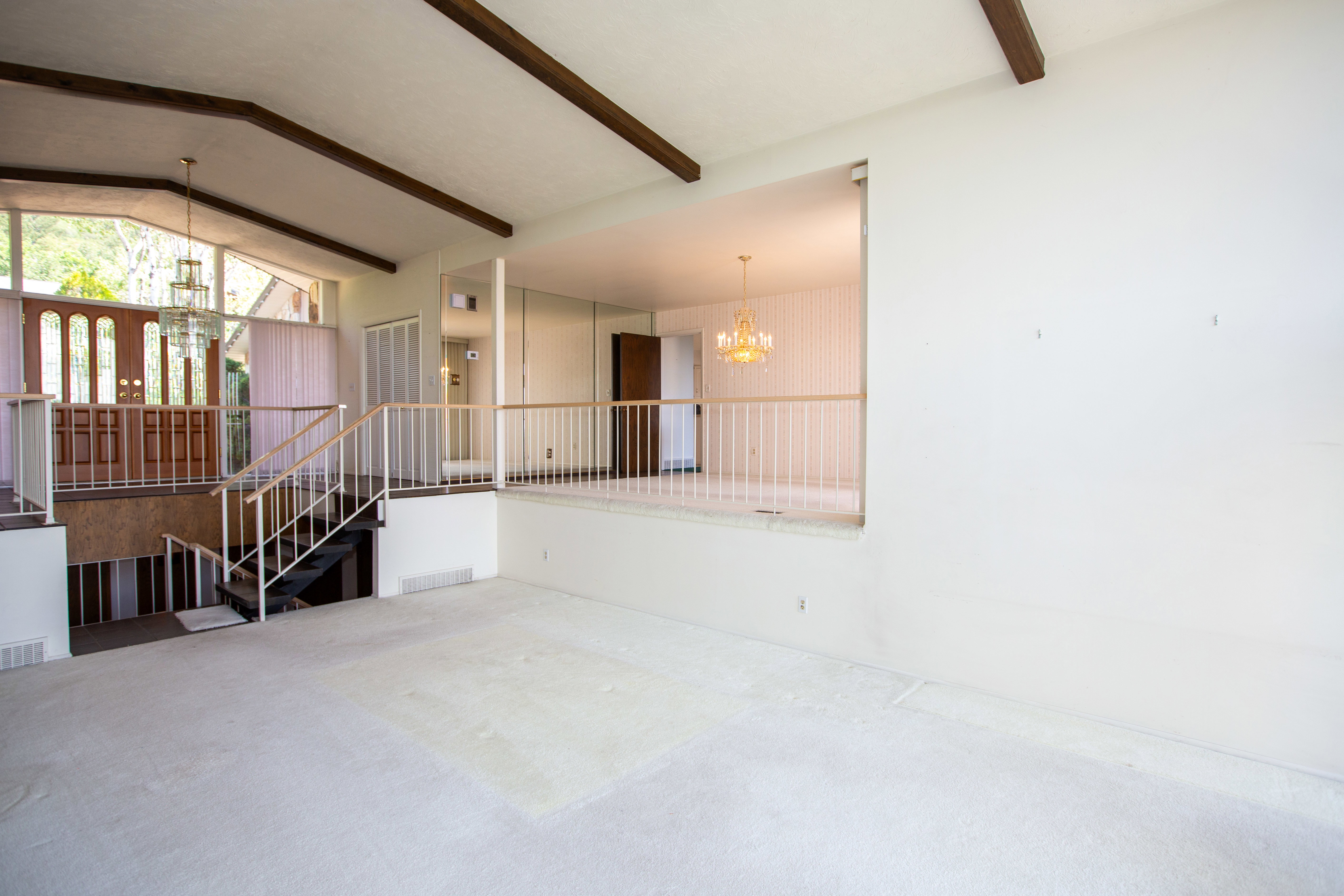 Split-level interior featuring a vaulted ceiling with exposed wood beams, a prominent staircase with white metal railings, and a tiered floor plan