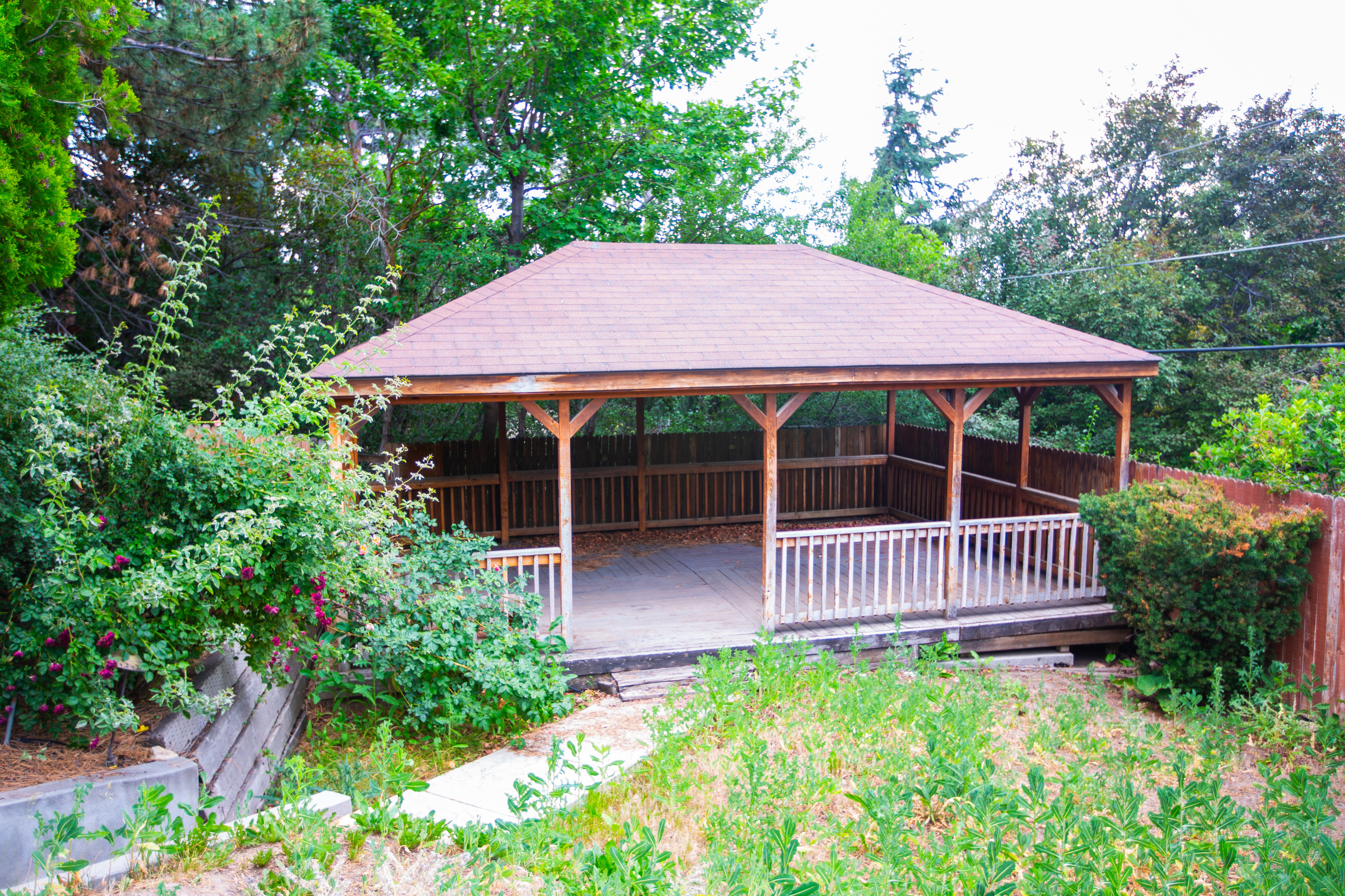 Expansive outdoor pavilion featuring a gabled roof, wood-finish support beams, and a surrounding wood railing