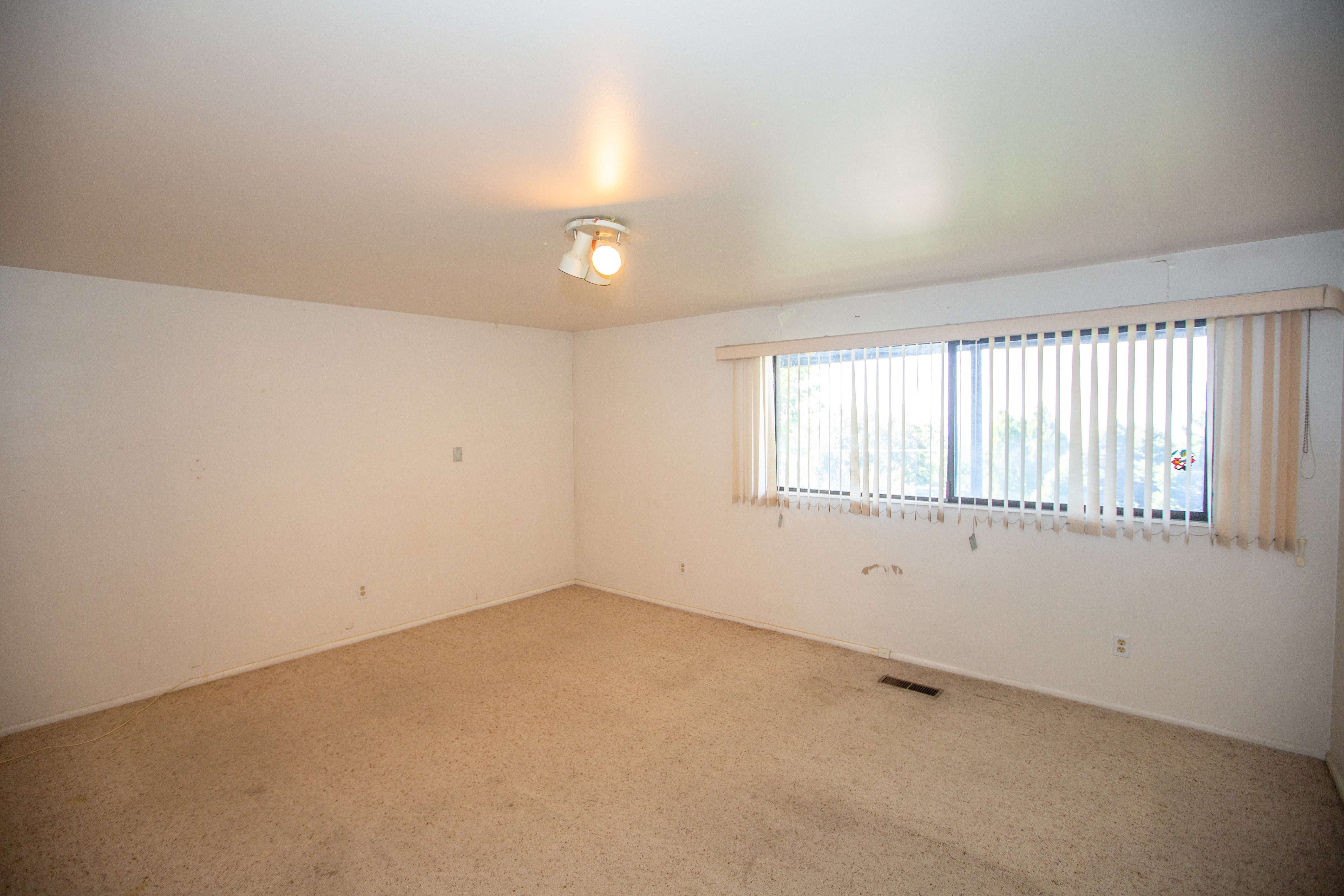 Bedroom featuring broadloom carpeting, track lighting, and a large window with vertical blinds