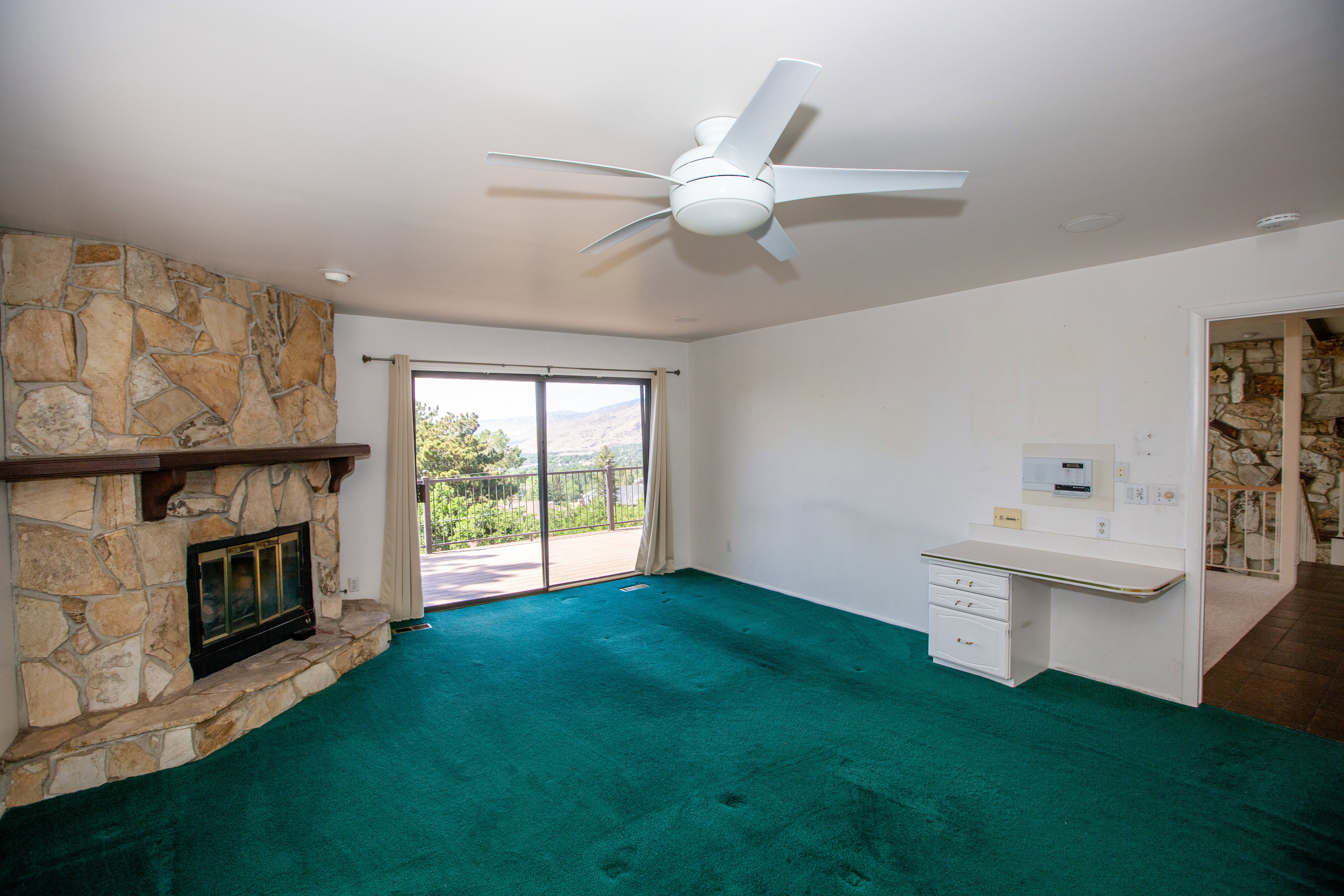Stone-clad fireplace with a wood mantle, sliding glass door to exterior, built-in desk cabinetry, and ceiling fan