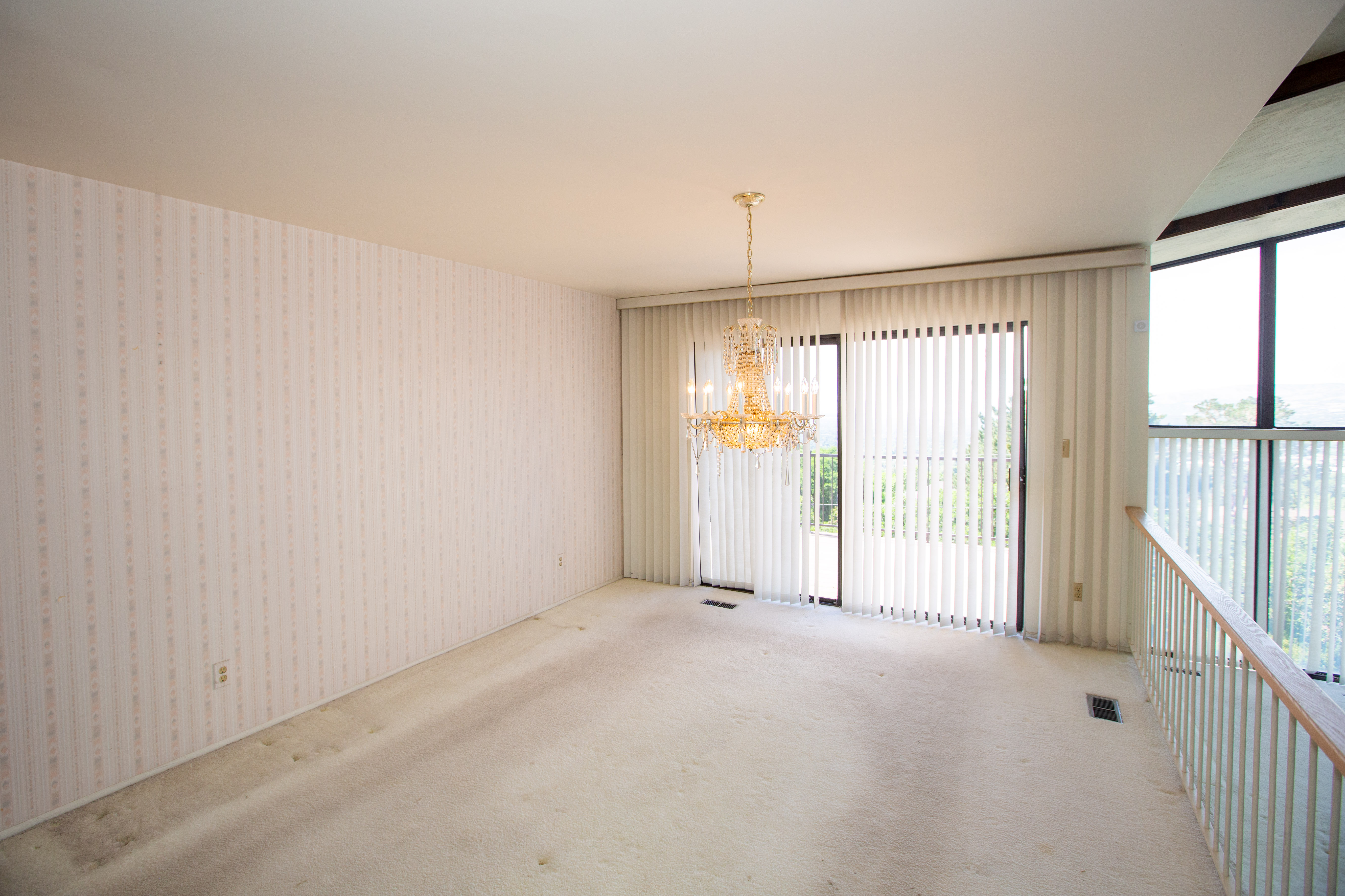 Spacious dining room with vertical blinds on expansive windows, a gold-toned chandelier, and patterned wallpaper
