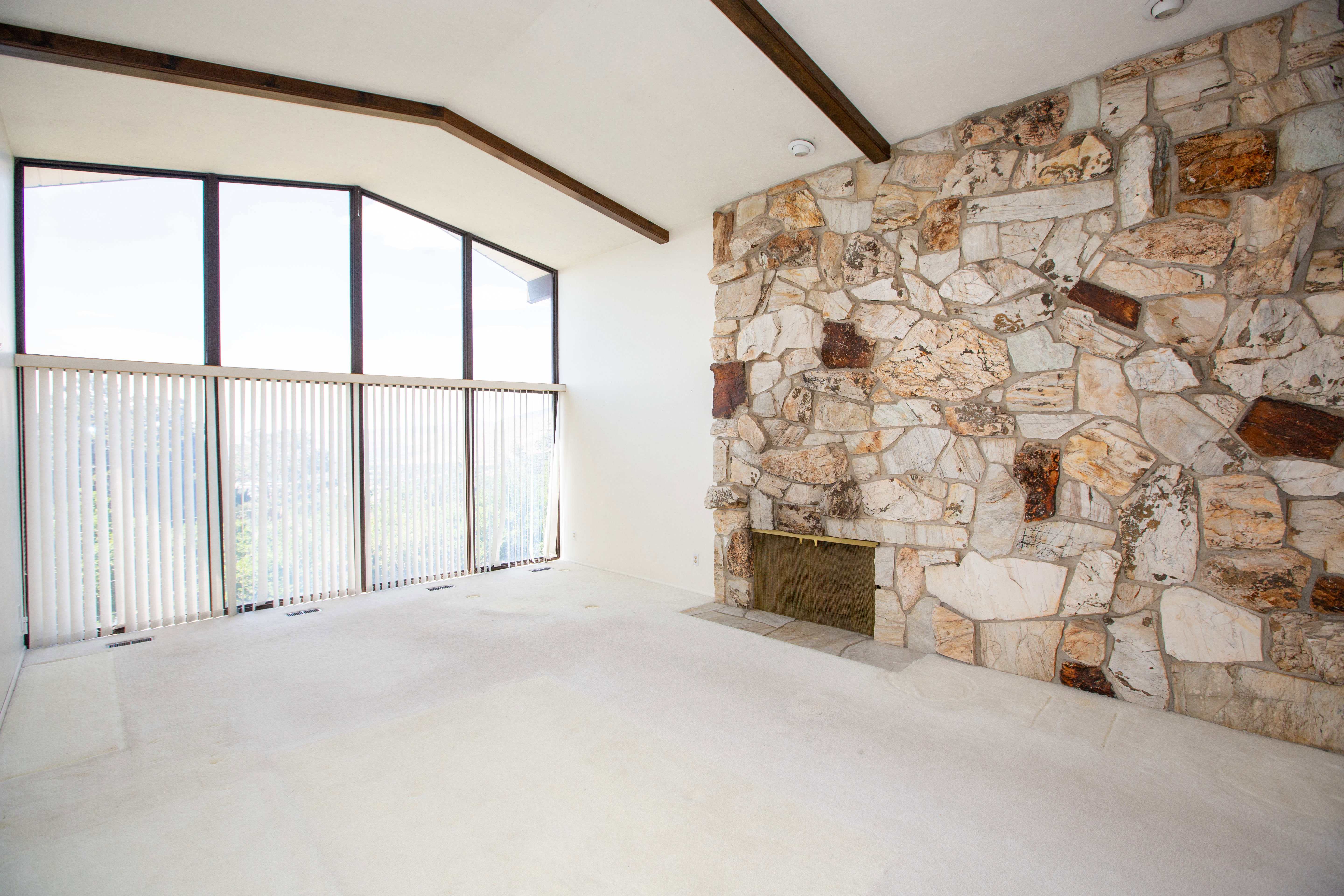 Spacious room featuring a floor-to-ceiling stone fireplace with a brass firebox
