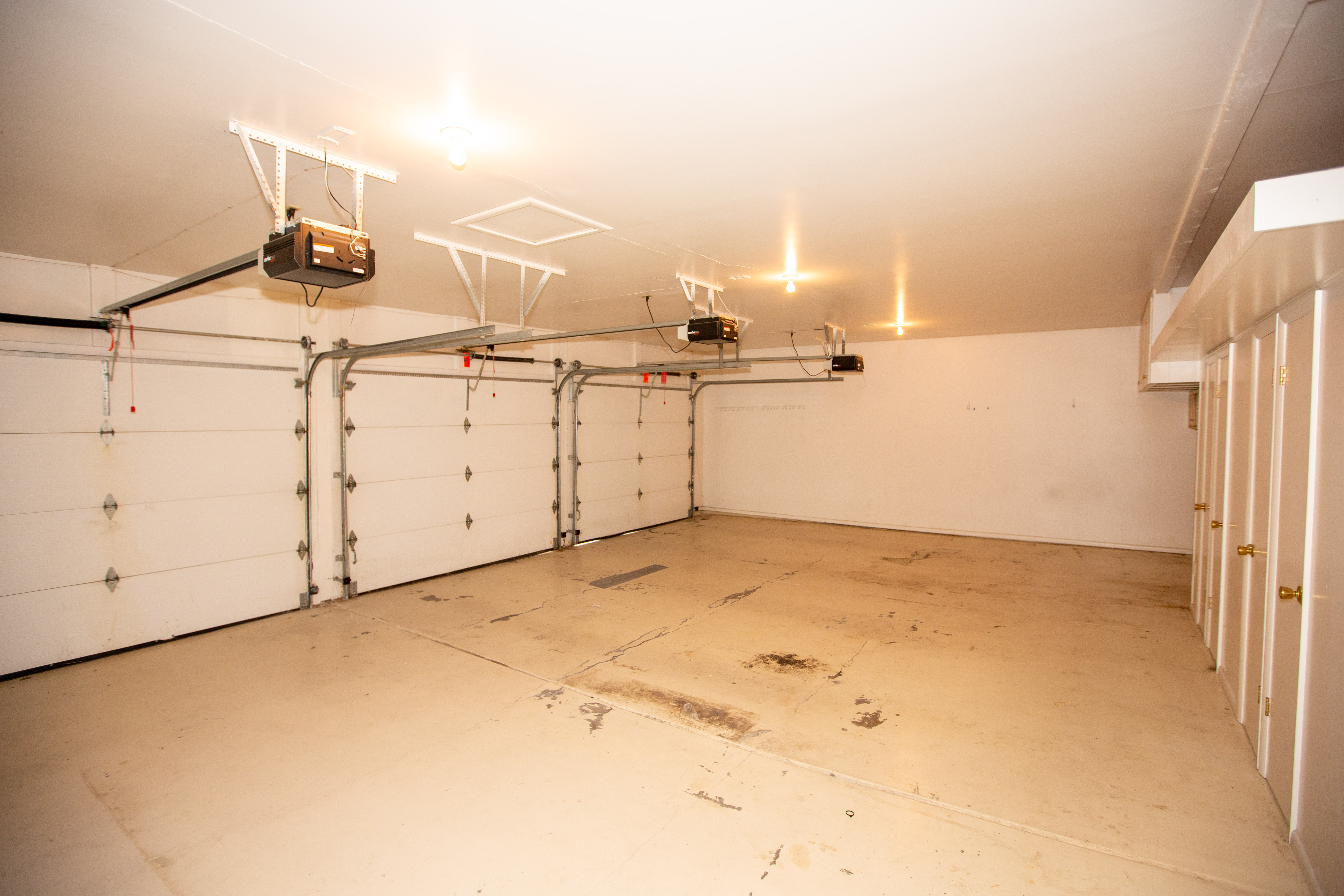Spacious garage featuring three overhead doors with automatic openers, concrete flooring, and multiple built-in storage cabinets