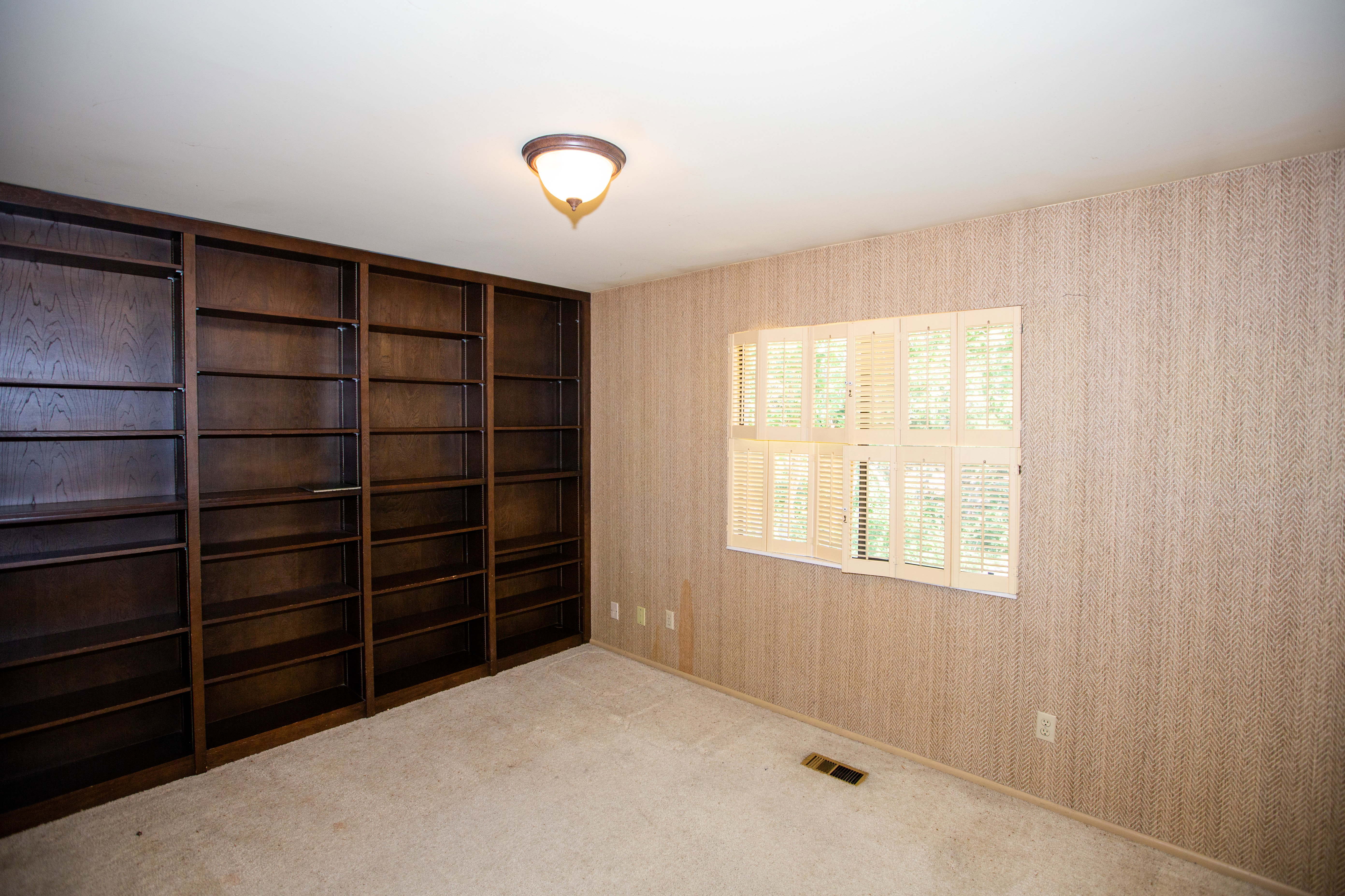Room featuring extensive built-in shelving, a window with louvered shutters, and textured wall coverings