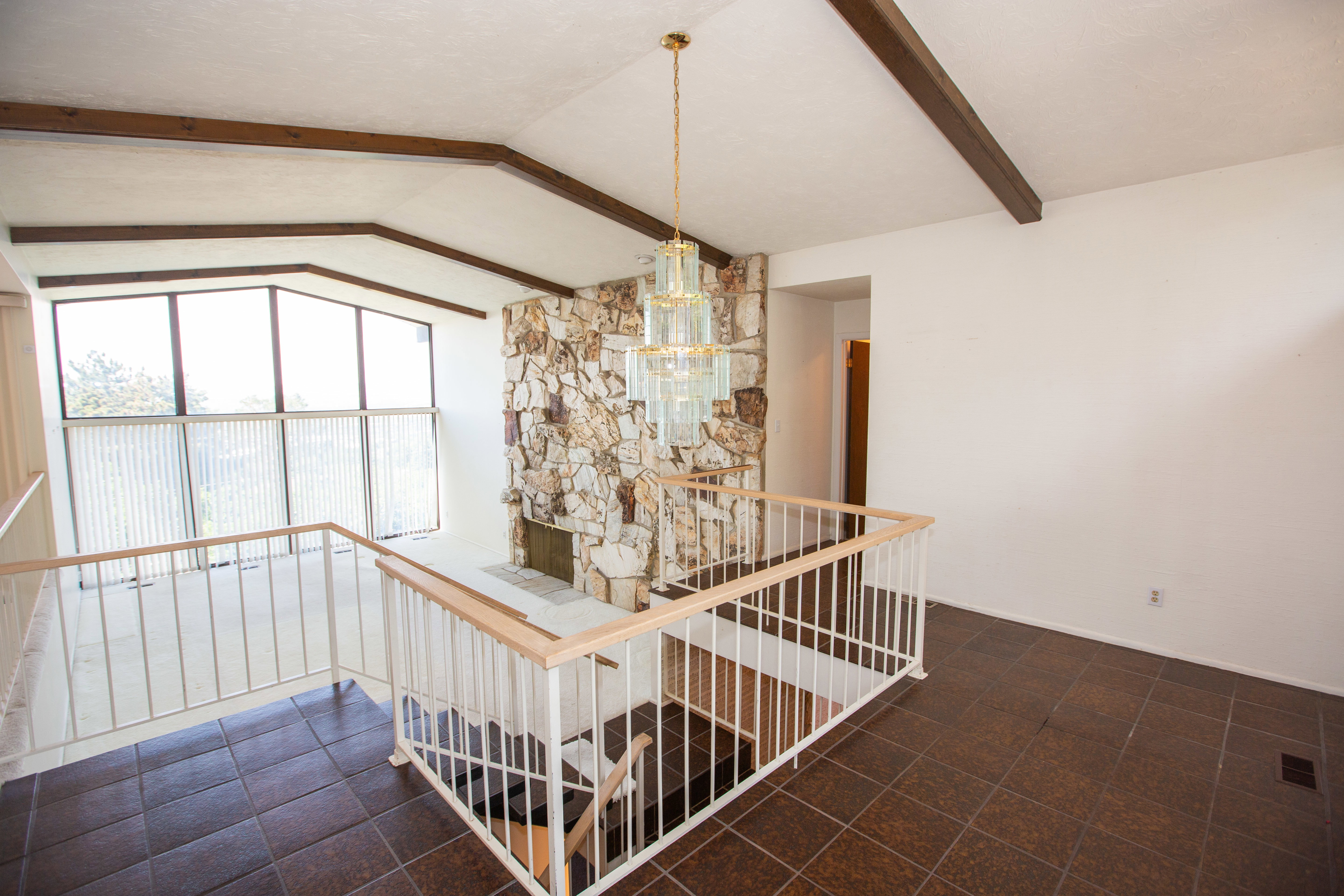 Great room featuring a natural stone fireplace, vaulted ceiling with exposed wood beams, and a tiered glass chandelier