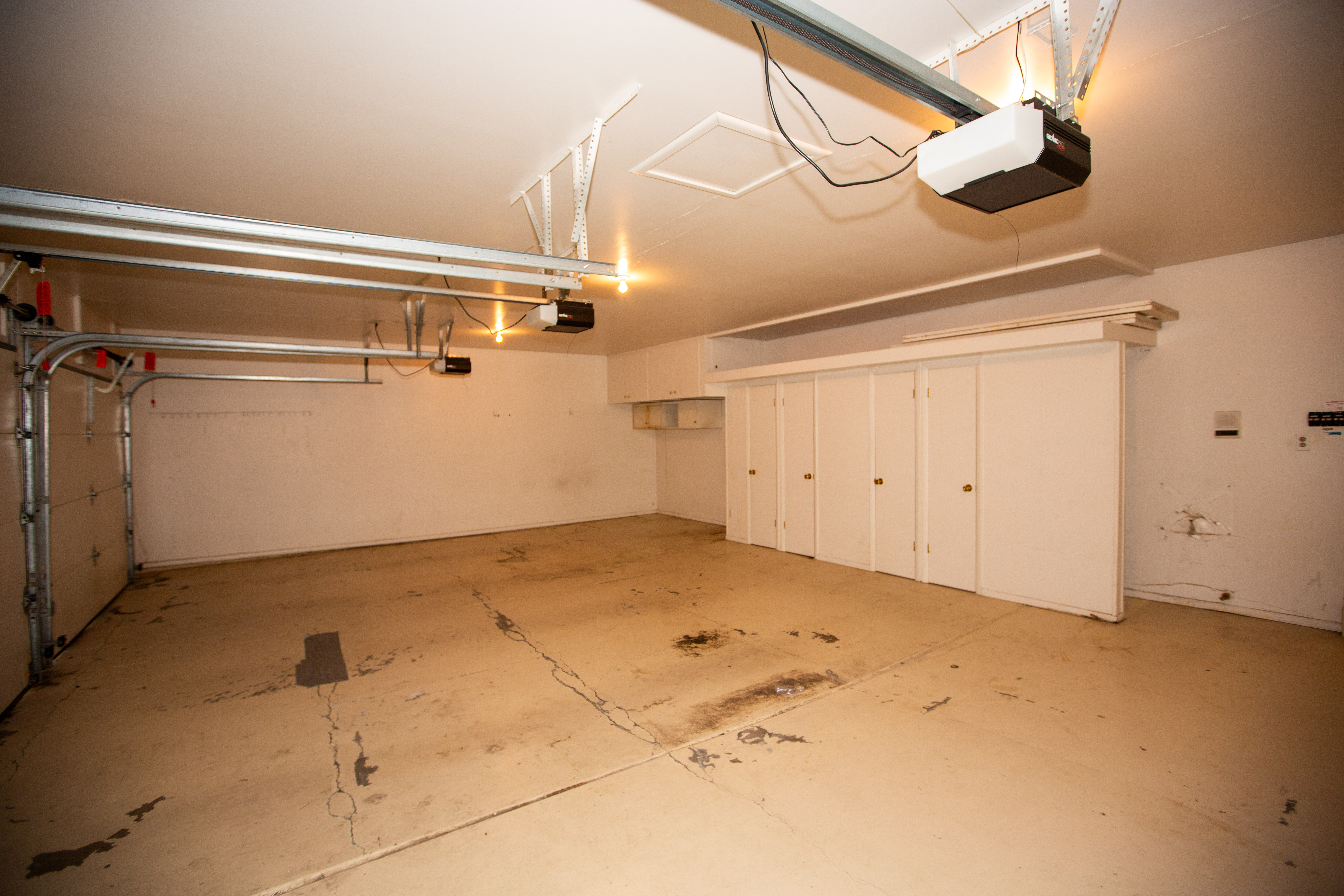 Spacious garage featuring an automatic door opener, overhead lighting, an expansive row of built-in cabinetry, and white painted walls