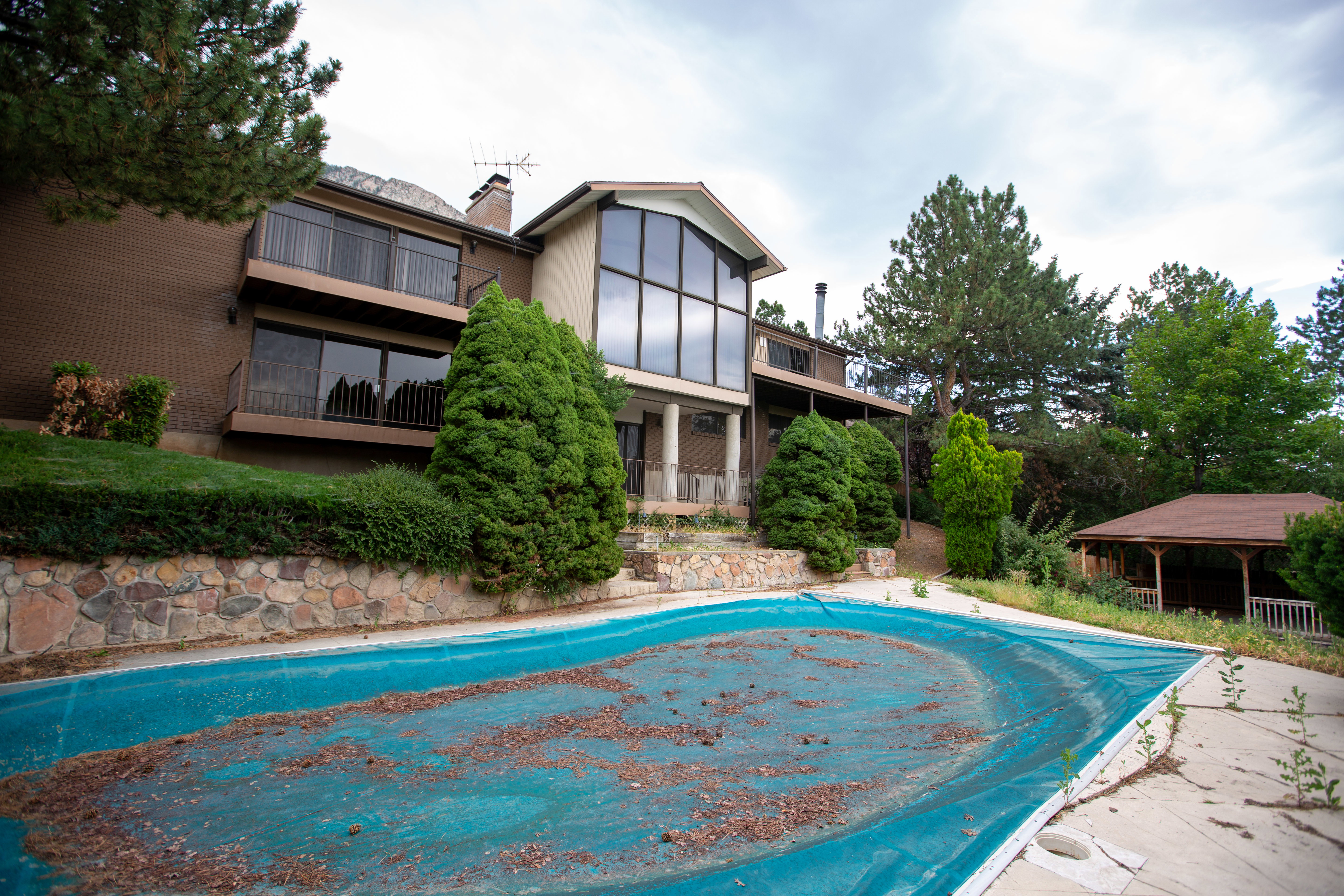 Multi-level exterior featuring a covered swimming pool, stone retaining wall, and mature landscaping
