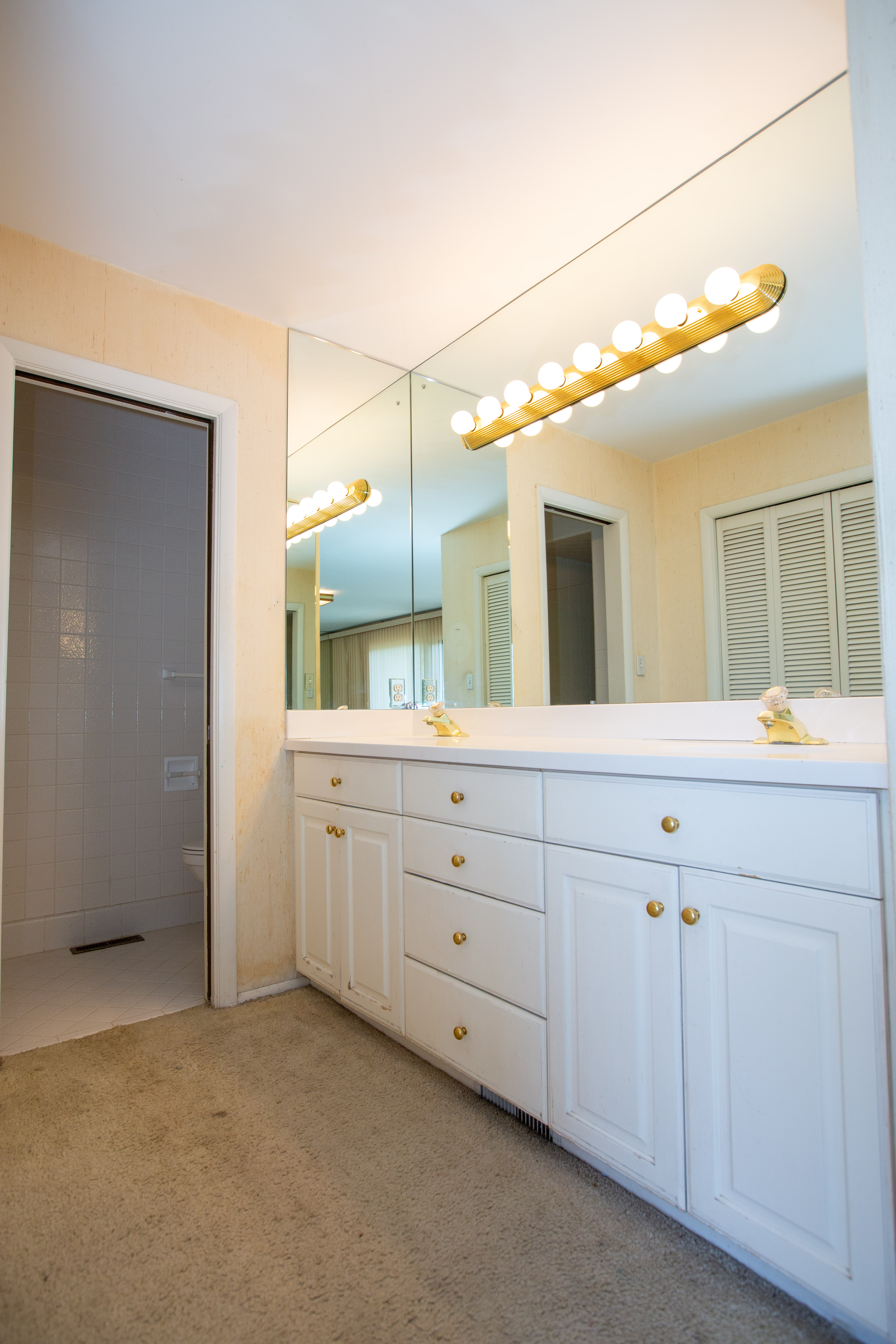 Master bathroom vanity featuring dual sinks, white cabinetry with gold-toned hardware, and an expansive wall-mounted mirror