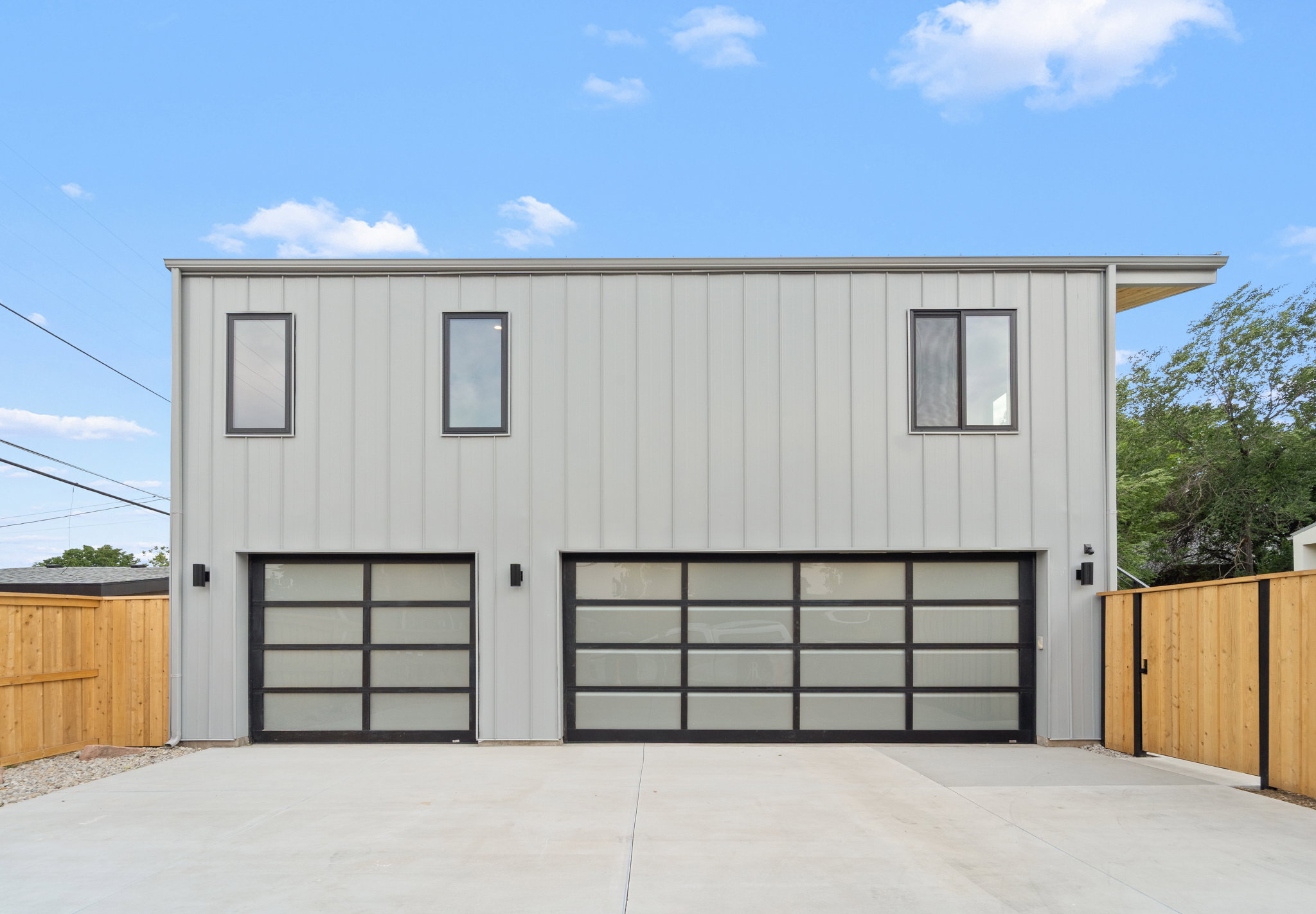 Contemporary two-story structure featuring vertical panel siding, two opaque glass garage doors, and a concrete driveway