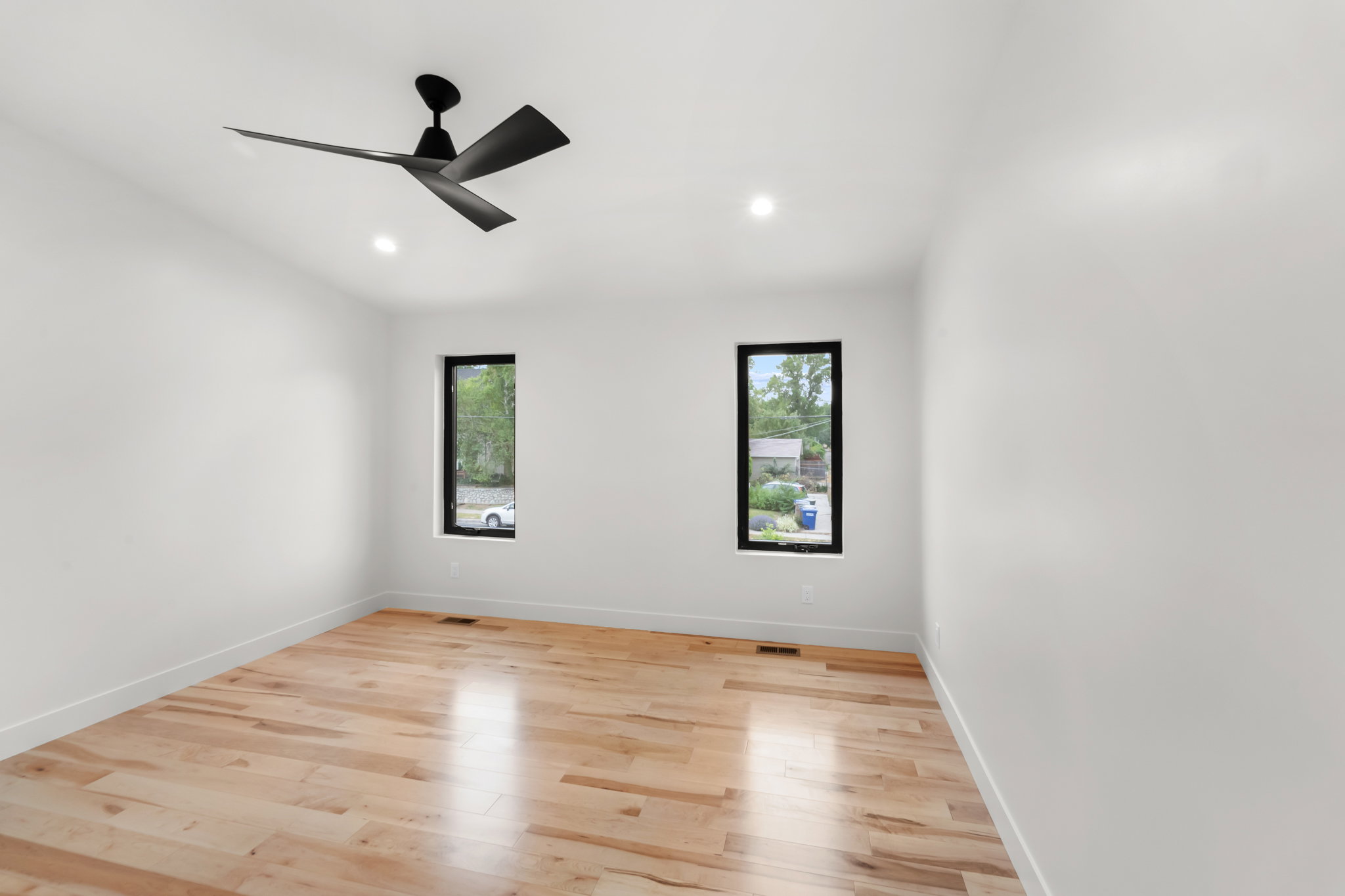 Bright room featuring wood-finish flooring, a modern matte black ceiling fan, recessed lighting, and two vertical windows with dark frames