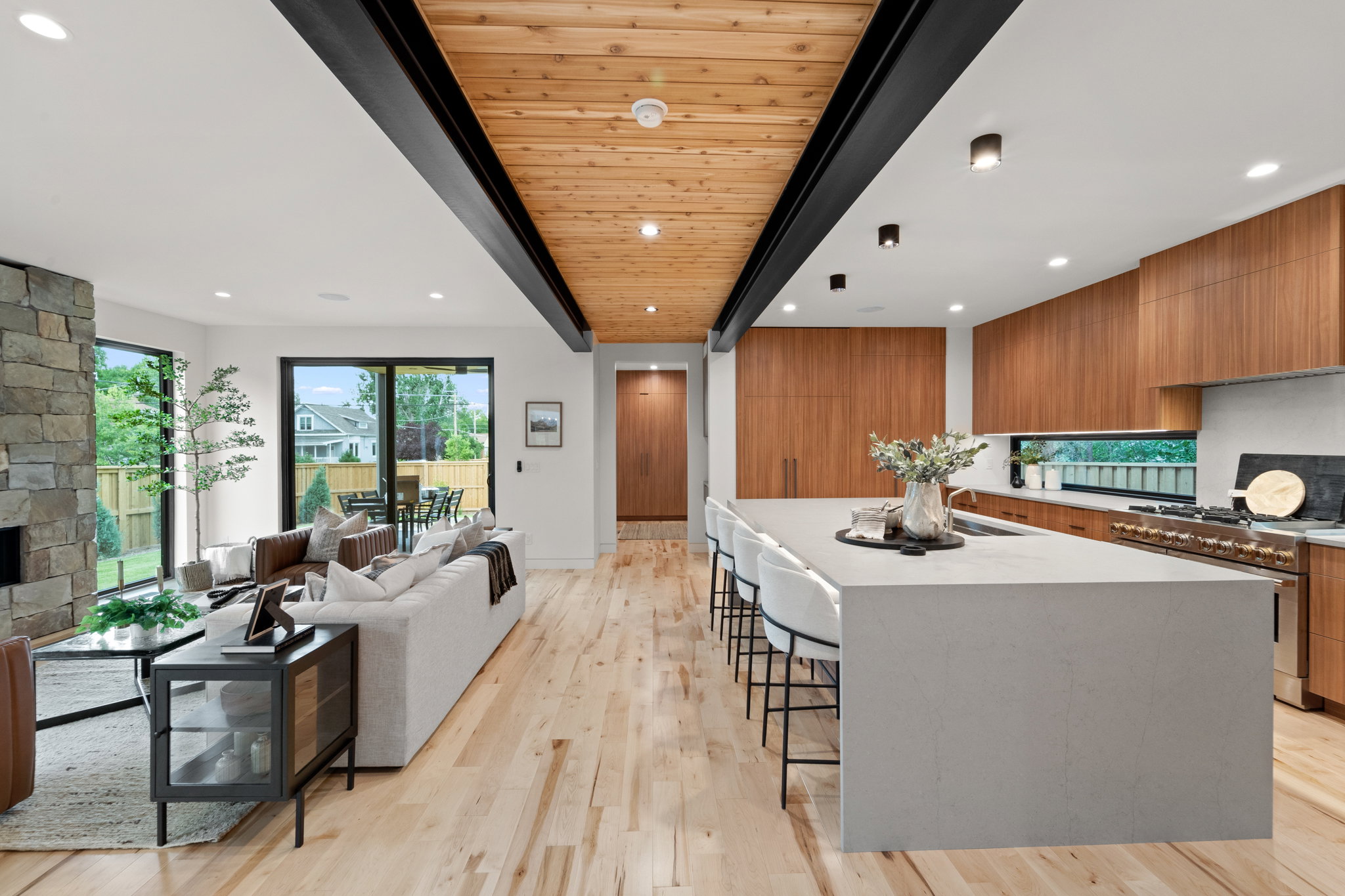 Open-concept interior featuring wood-finish flooring, a stone-clad fireplace, and a kitchen with a large island and integrated appliances