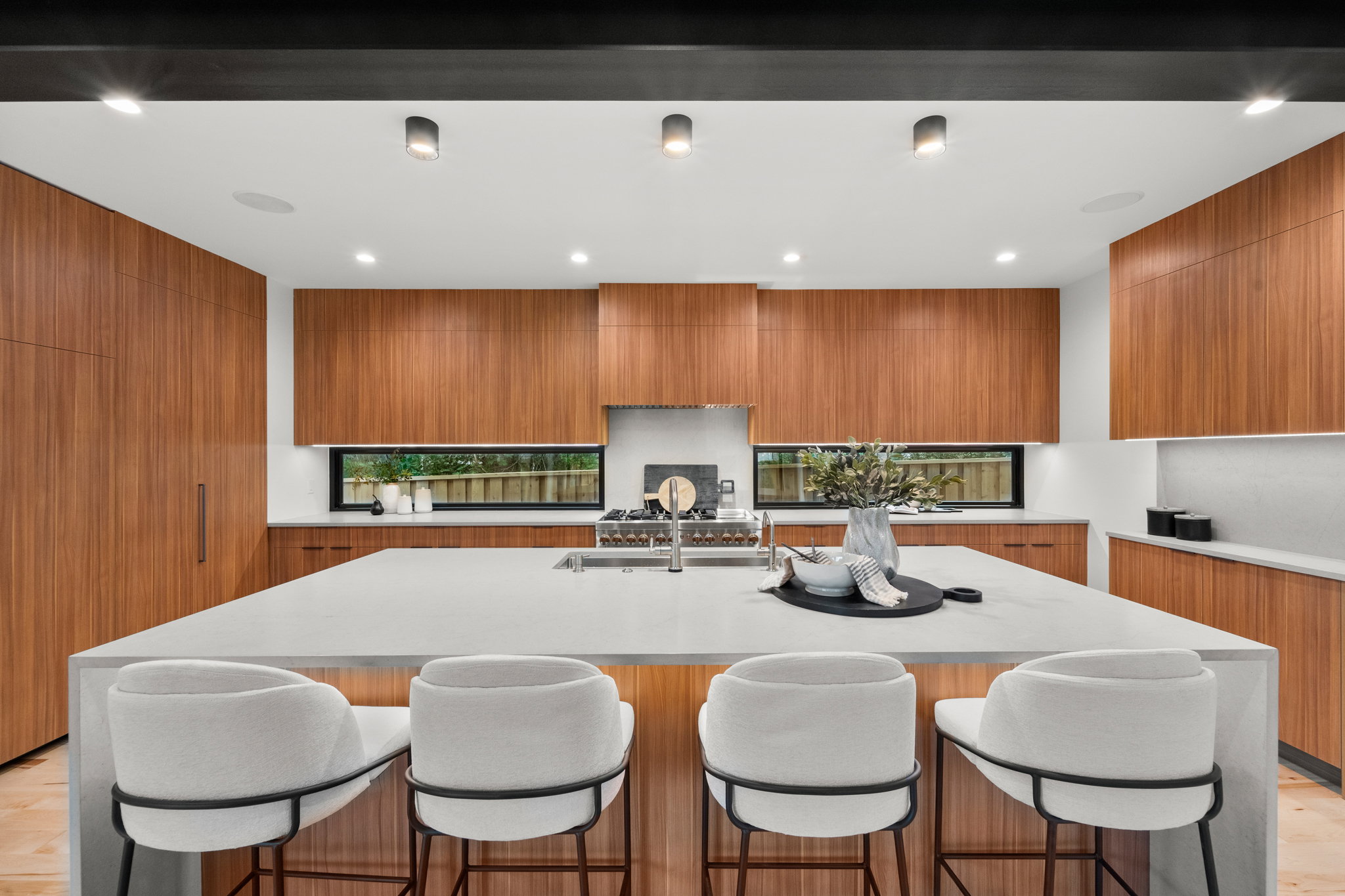 Gourmet kitchen featuring a substantial island with seating, integrated stainless steel appliances, extensive wood-finish cabinetry, sleek under-cabinet lighting, and a linear window backsplash