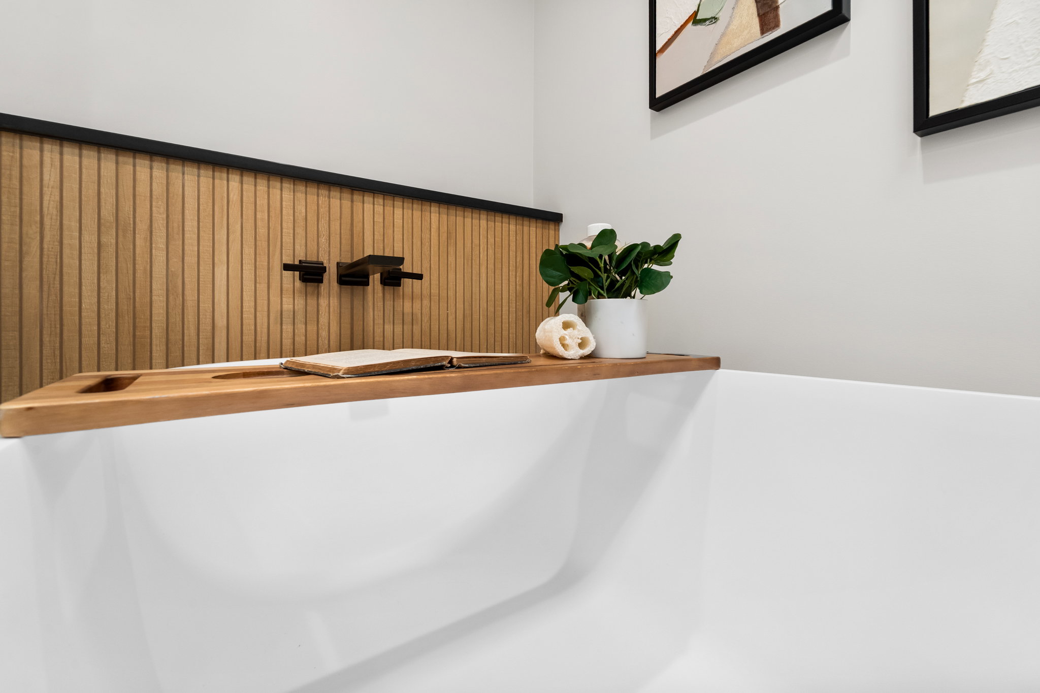 Freestanding white soaking tub with a wall-mounted matte black faucet, set against a wood-paneled accent wall