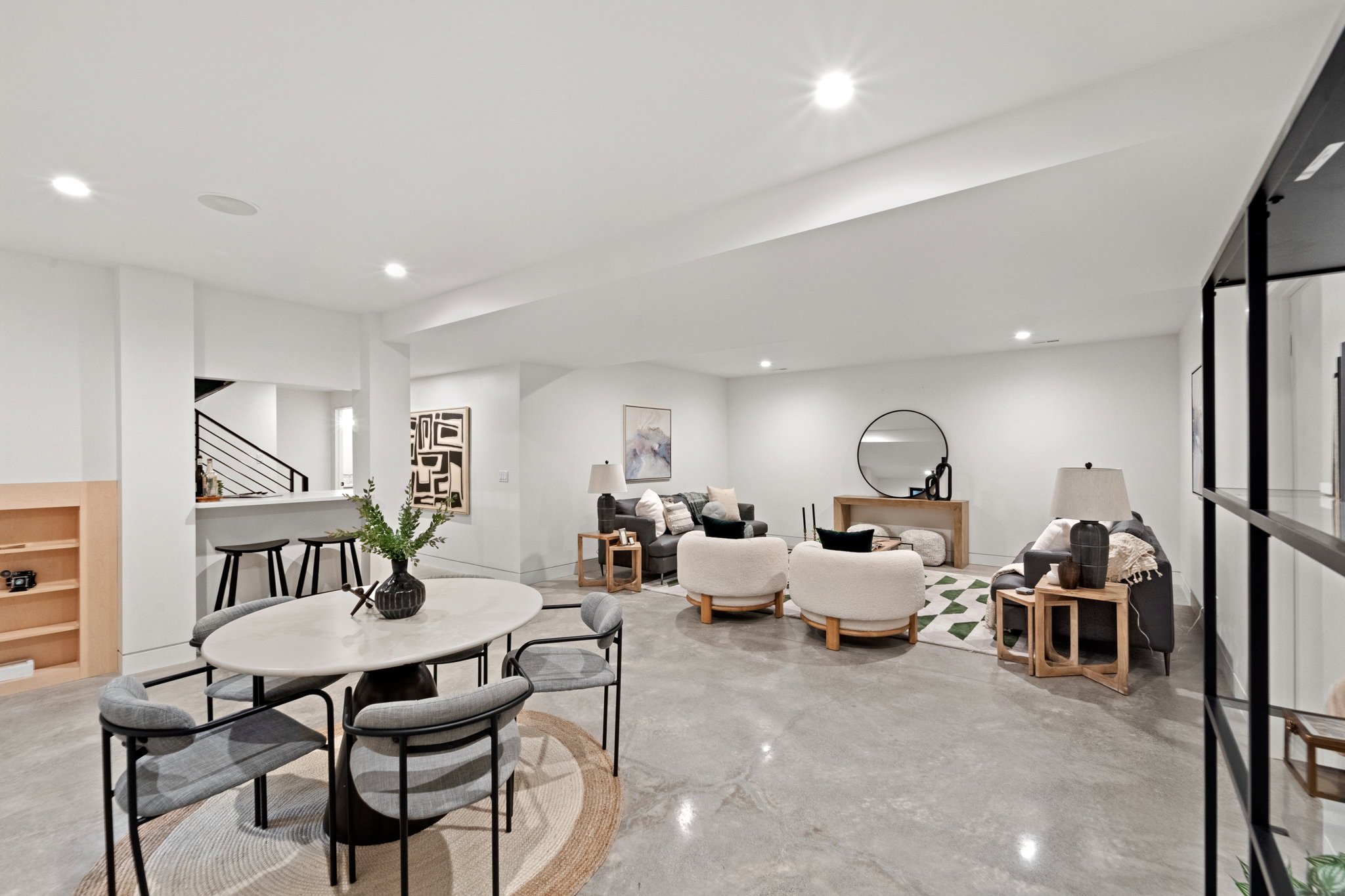 Spacious open concept room featuring polished concrete flooring, recessed lighting, a built-in bar with pendant lighting, a partial wood-finish built-in shelving unit, and a black metal and glass partition
