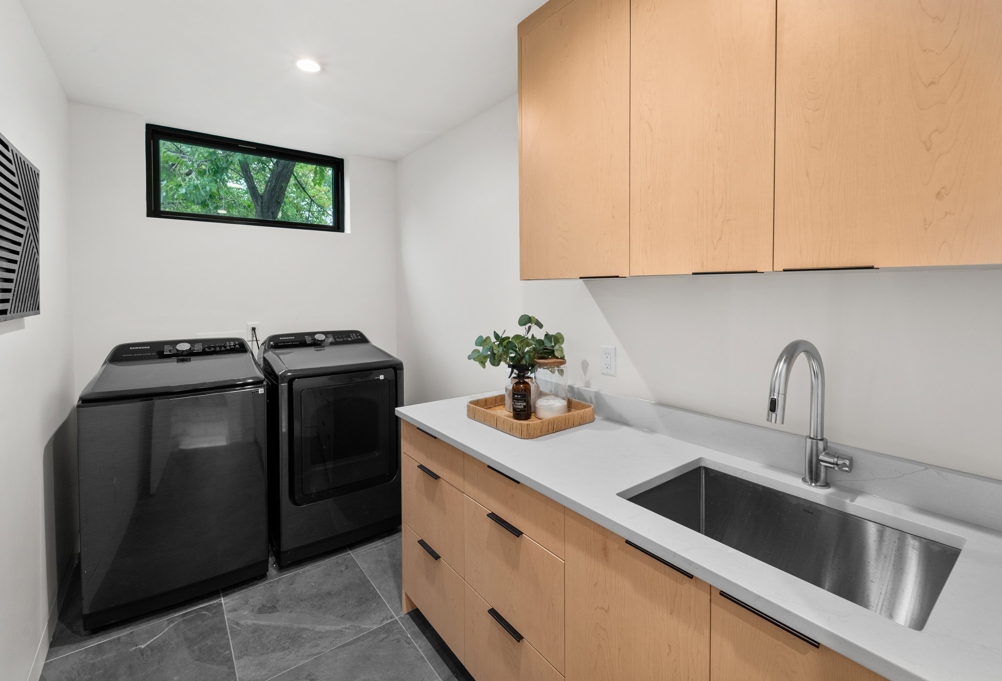 Dedicated laundry room featuring light wood-finish cabinetry, a stainless steel sink, and light stone-finish countertops