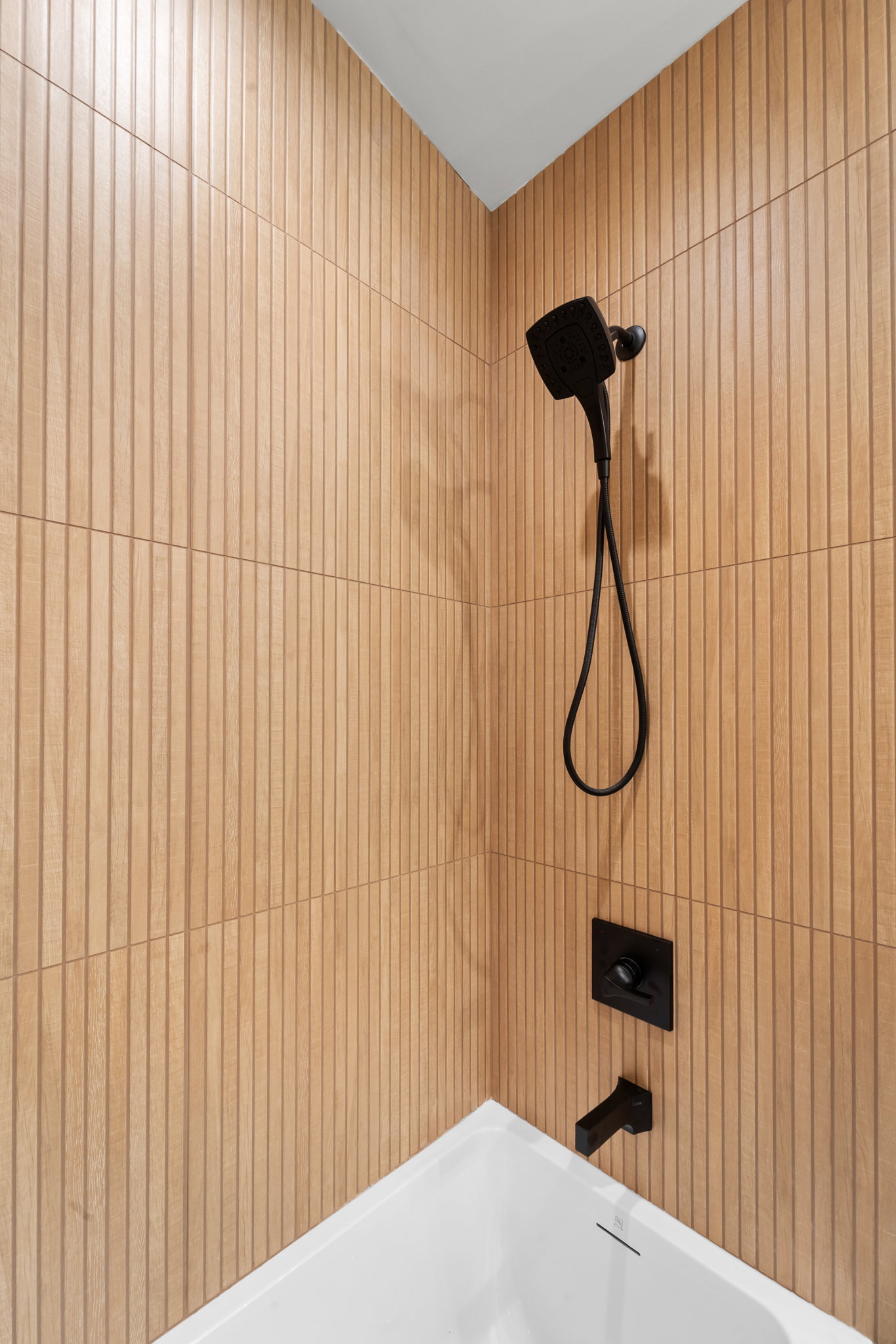Shower and tub combination featuring wood-look tile surround and matte black fixtures