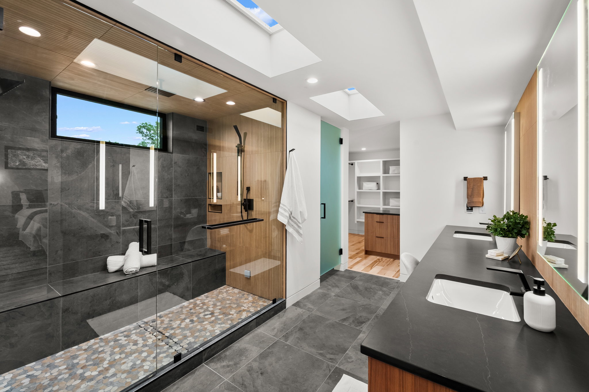 Spacious bathroom featuring a glass-enclosed shower with stone tile walls, a built-in bench, and pebble flooring