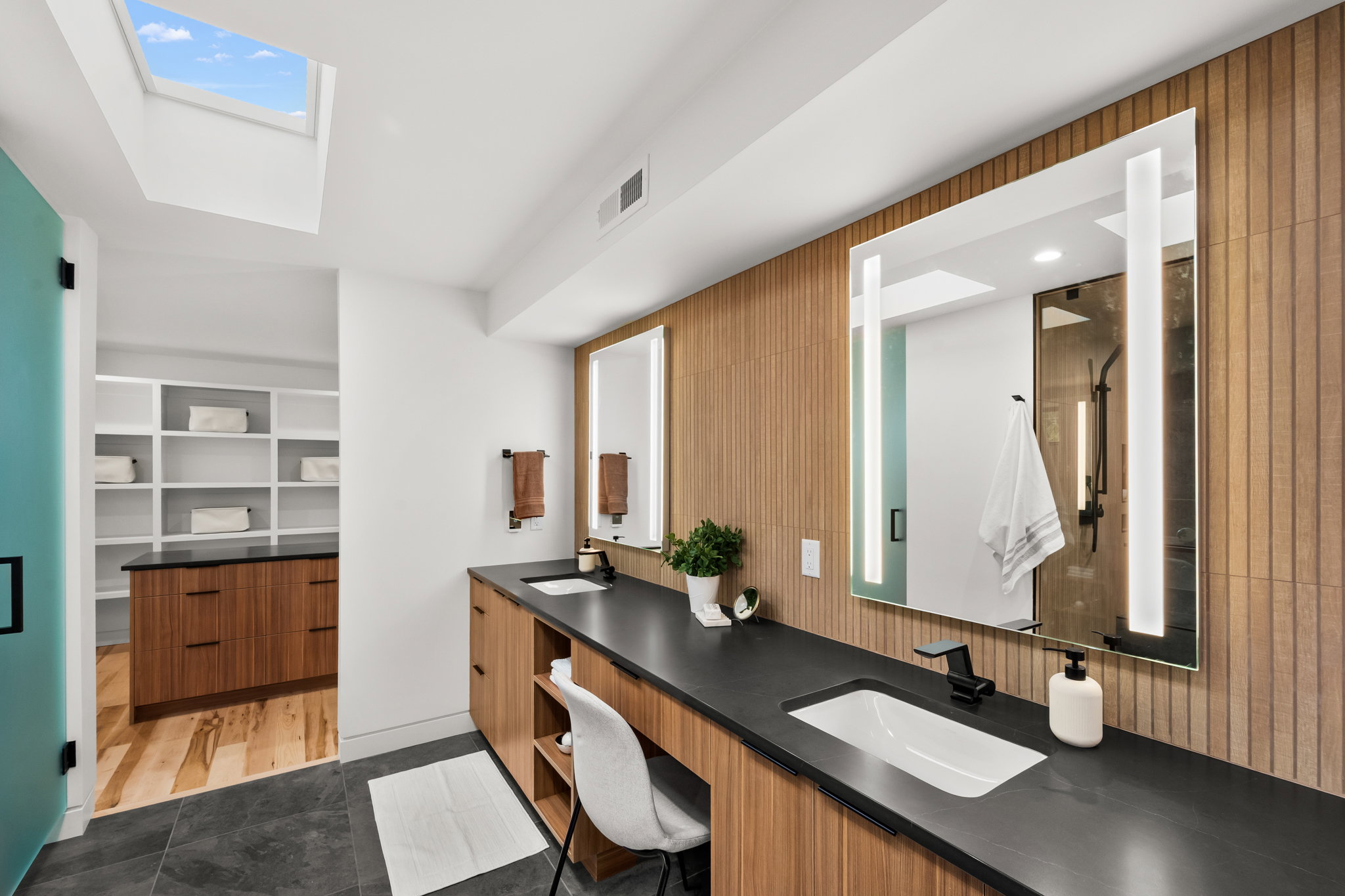 Contemporary bathroom featuring a skylight, dual vanity with wood-finish cabinetry, black countertops, and integrated rectangular sinks