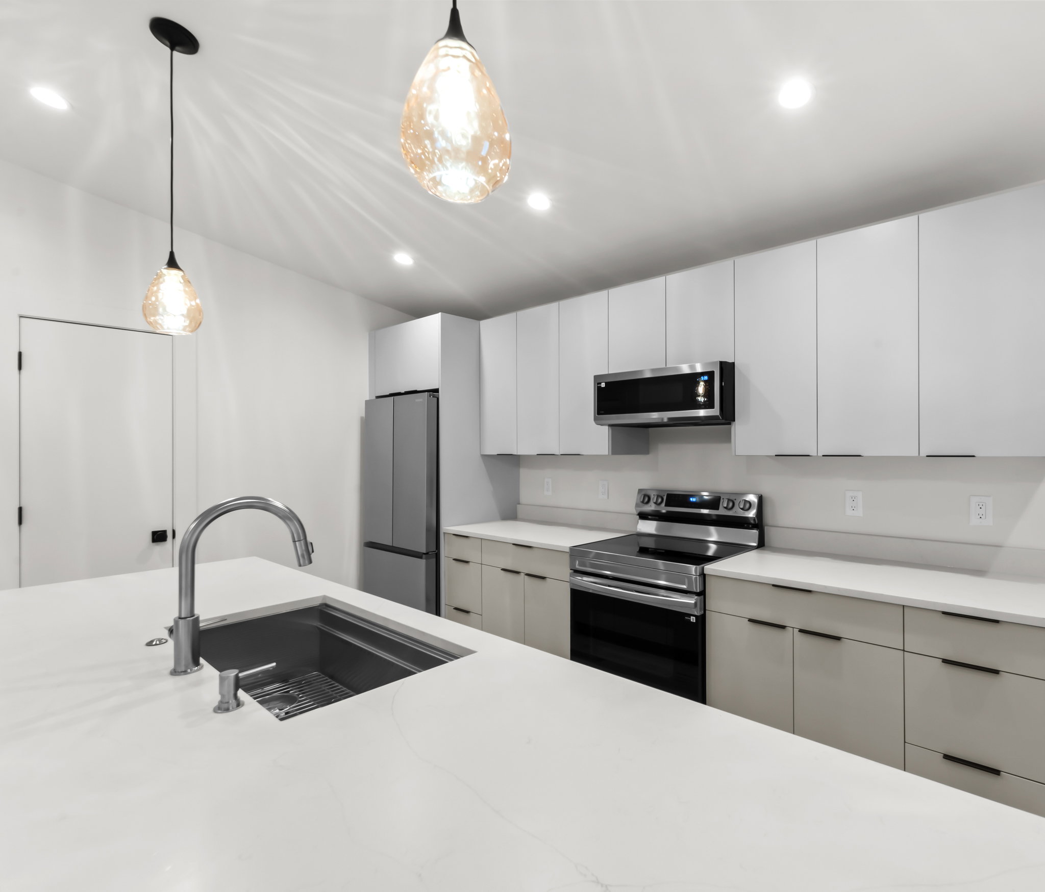 Modern kitchen featuring white cabinetry, stainless steel appliances, a large island with an undermount sink, pendant lighting, and recessed ceiling lights