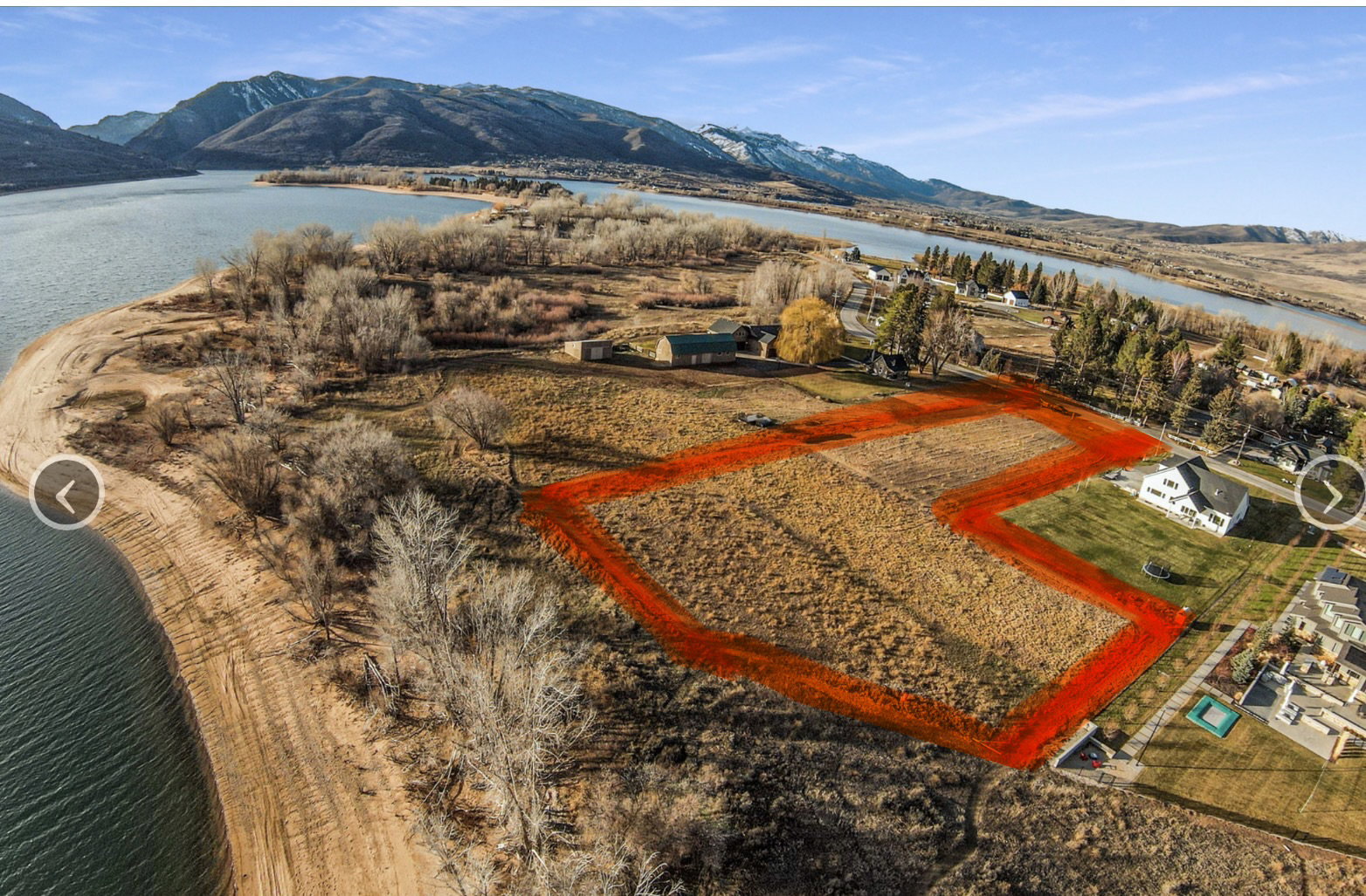 Expansive land parcel with water frontage, featuring a clear, buildable area and distant mountain backdrop