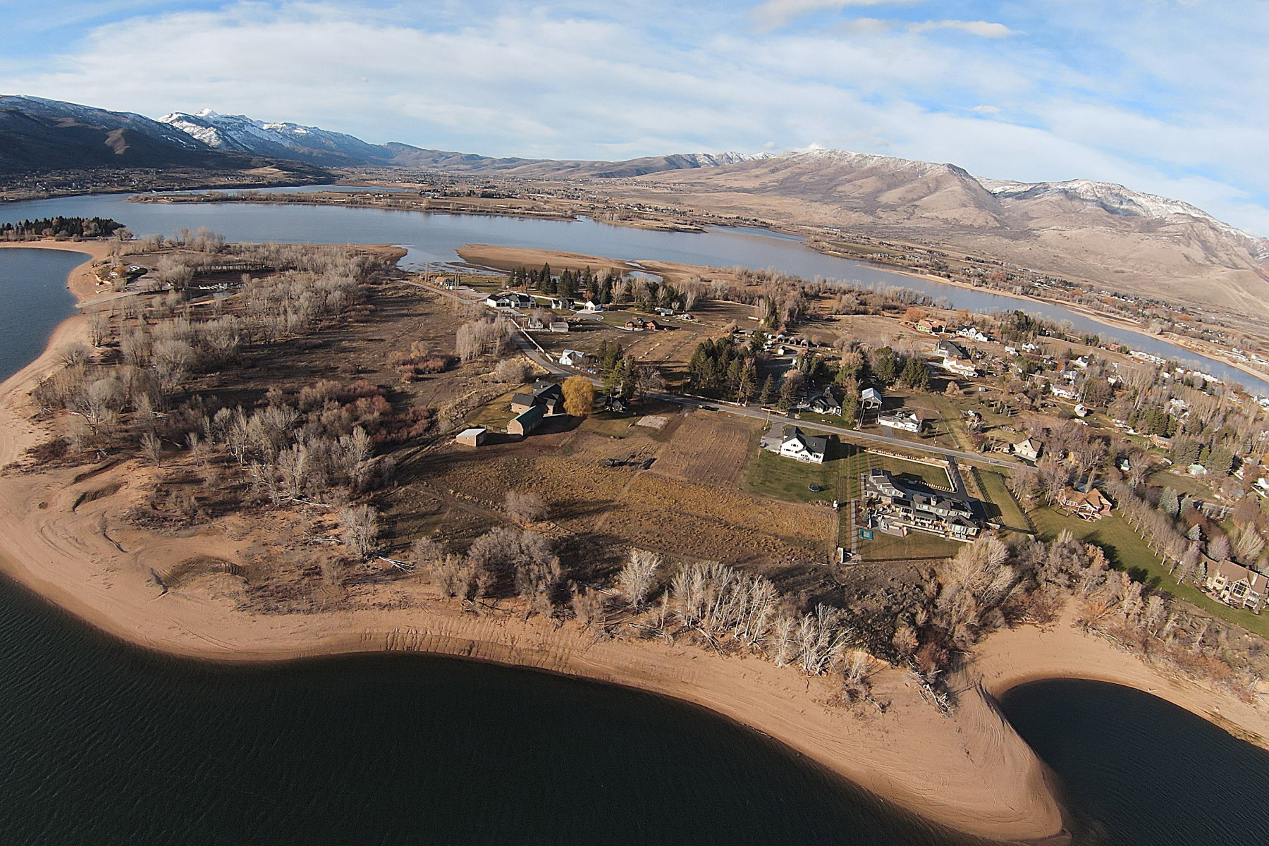Aerial perspective showcasing a property situated along a substantial body of water, featuring a varied landscape with distant snow-capped mountains