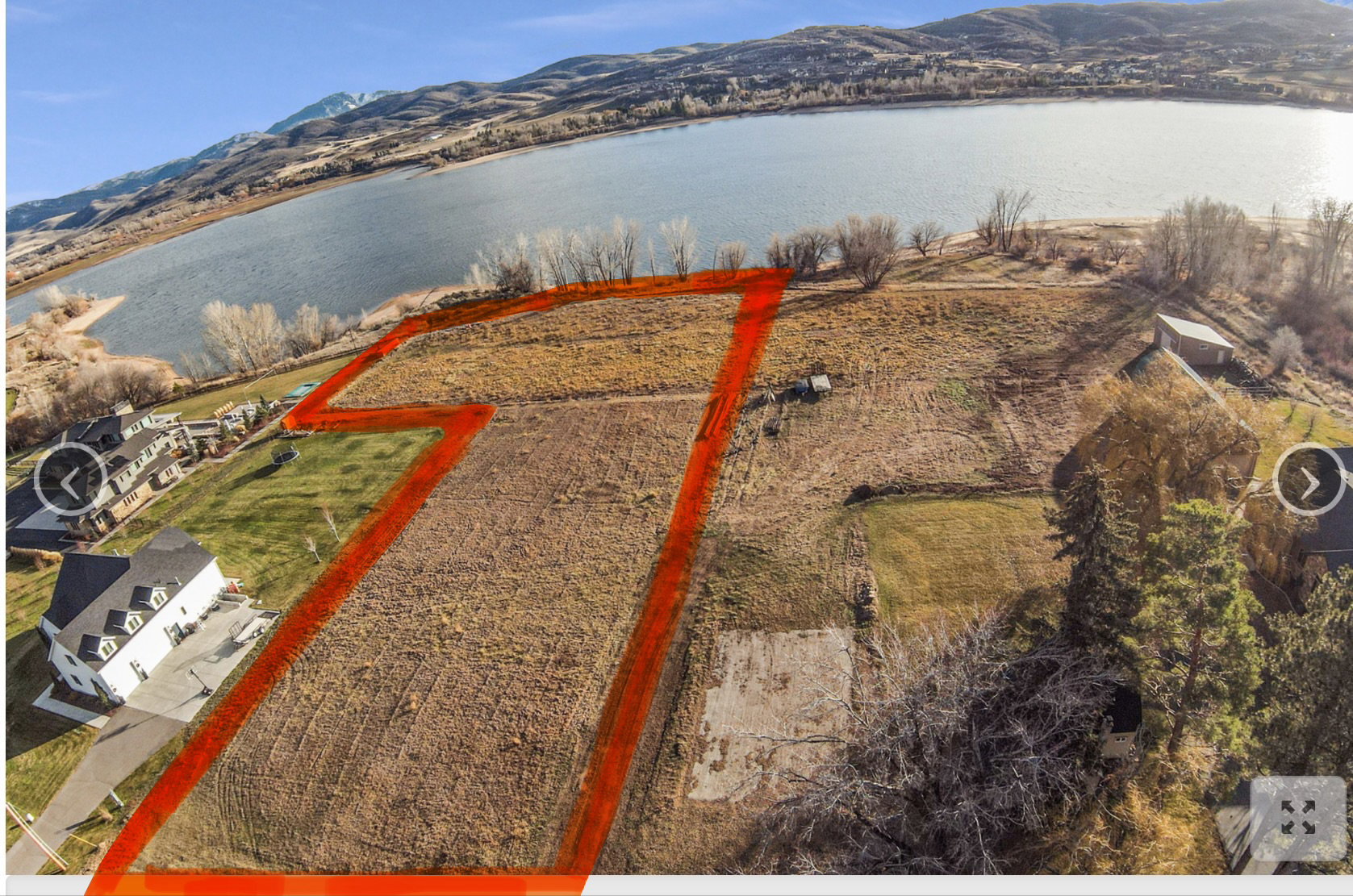 Expansive undeveloped land parcel featuring a shoreline, surrounding hills, and a clear water body