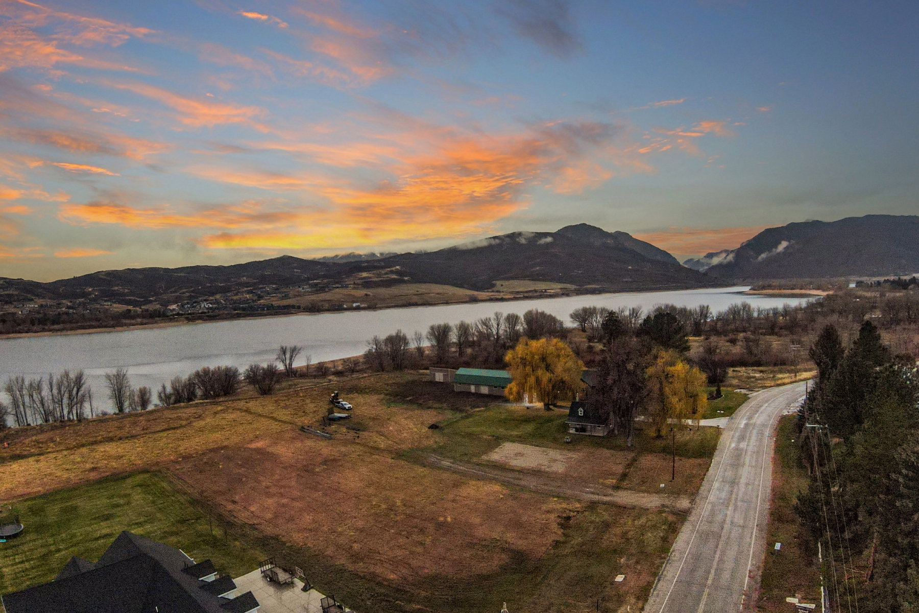 Expansive waterfront lot featuring a winding road, mature trees, and mountainous backdrop