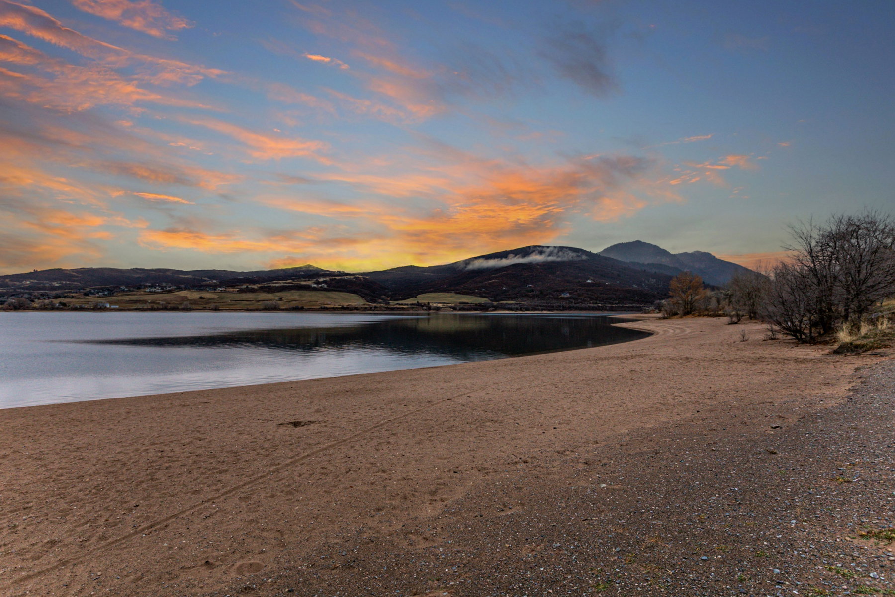 Expansive sandy shoreline bordering a tranquil body of water, with distant mountains providing a natural backdrop