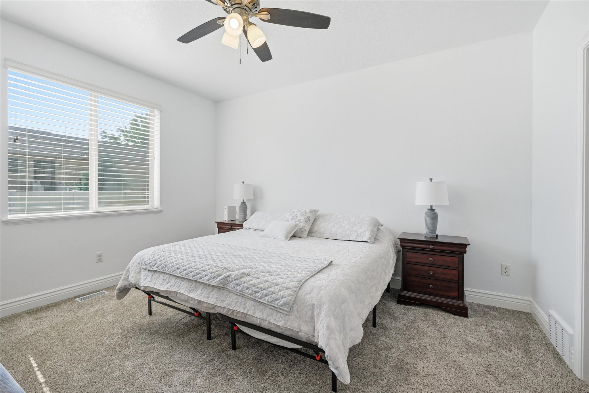 Bright room featuring a large window with blinds, a ceiling fan with integrated lighting, plush carpet flooring, white walls, and white baseboards