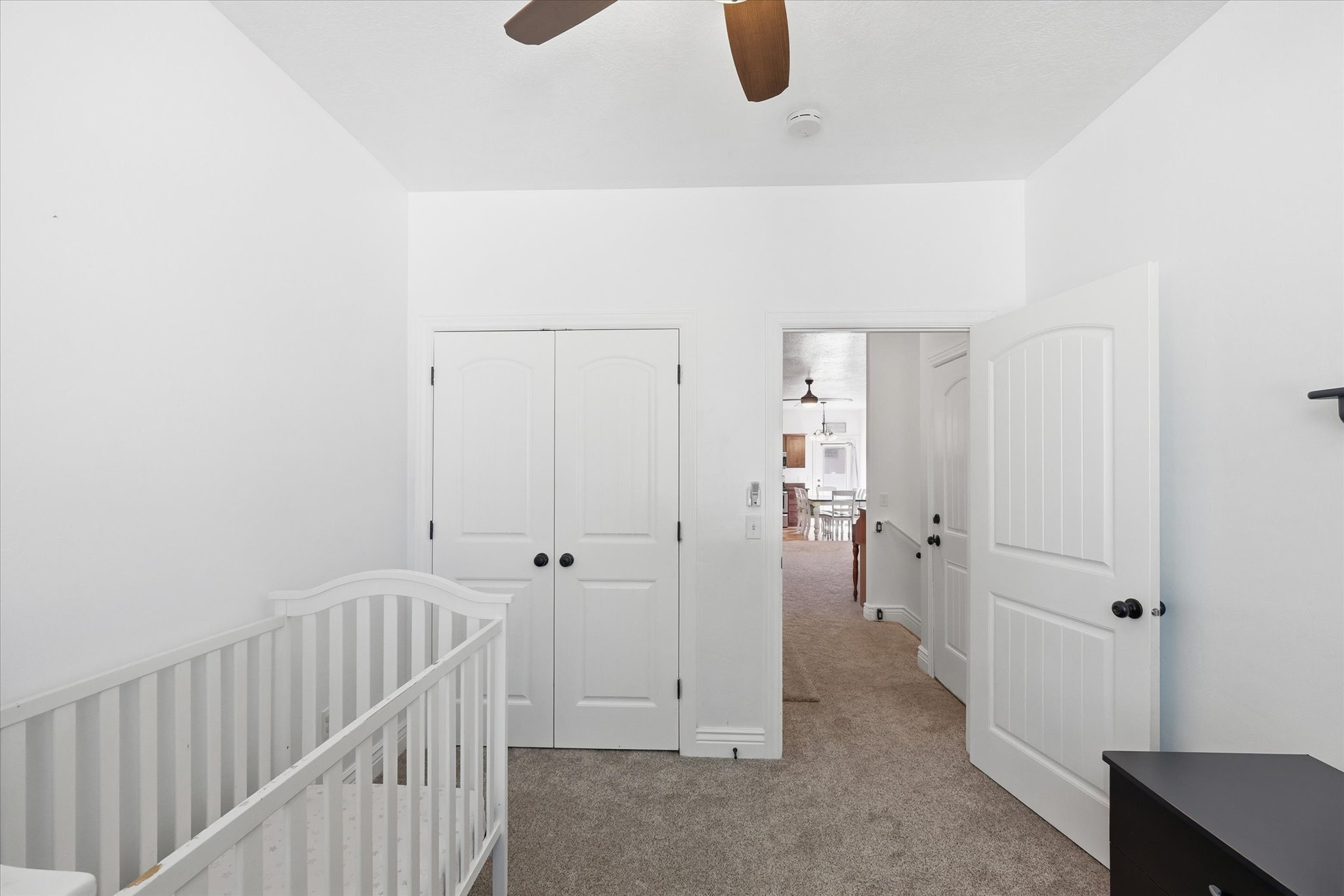 Room featuring neutral carpeting, white interior walls, and a ceiling fan with wood-finish blades