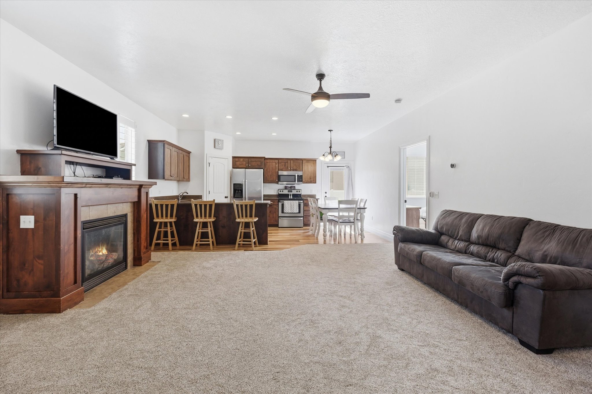 Open-concept living space featuring a built-in fireplace with a wood mantel, a kitchen island with seating, dark wood cabinetry, and stainless steel appliances