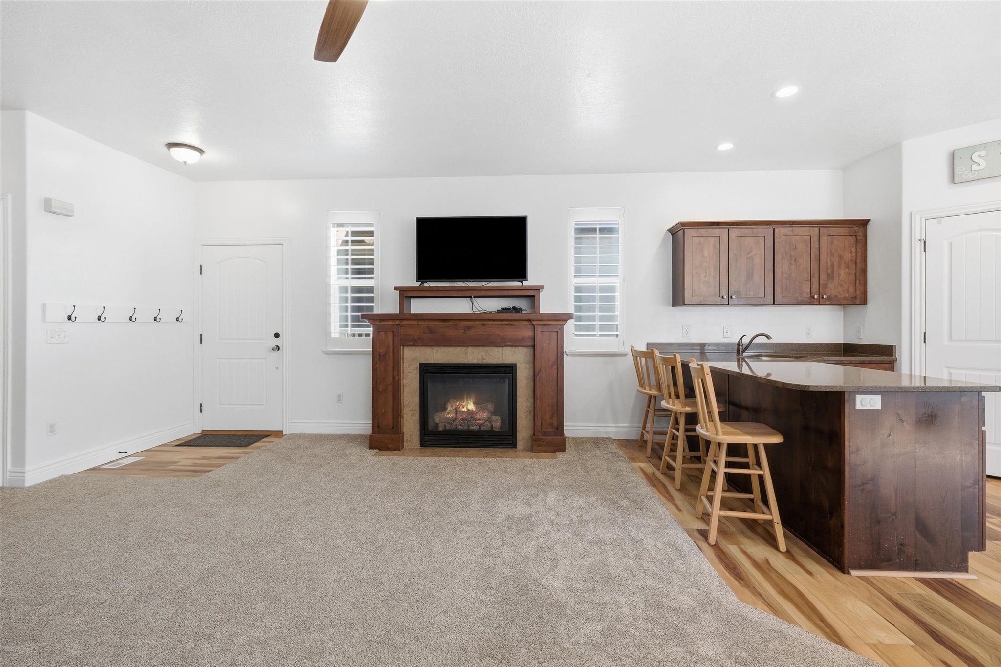 Living area featuring a stone-faced fireplace with wood mantel, ceiling fan, and carpet flooring