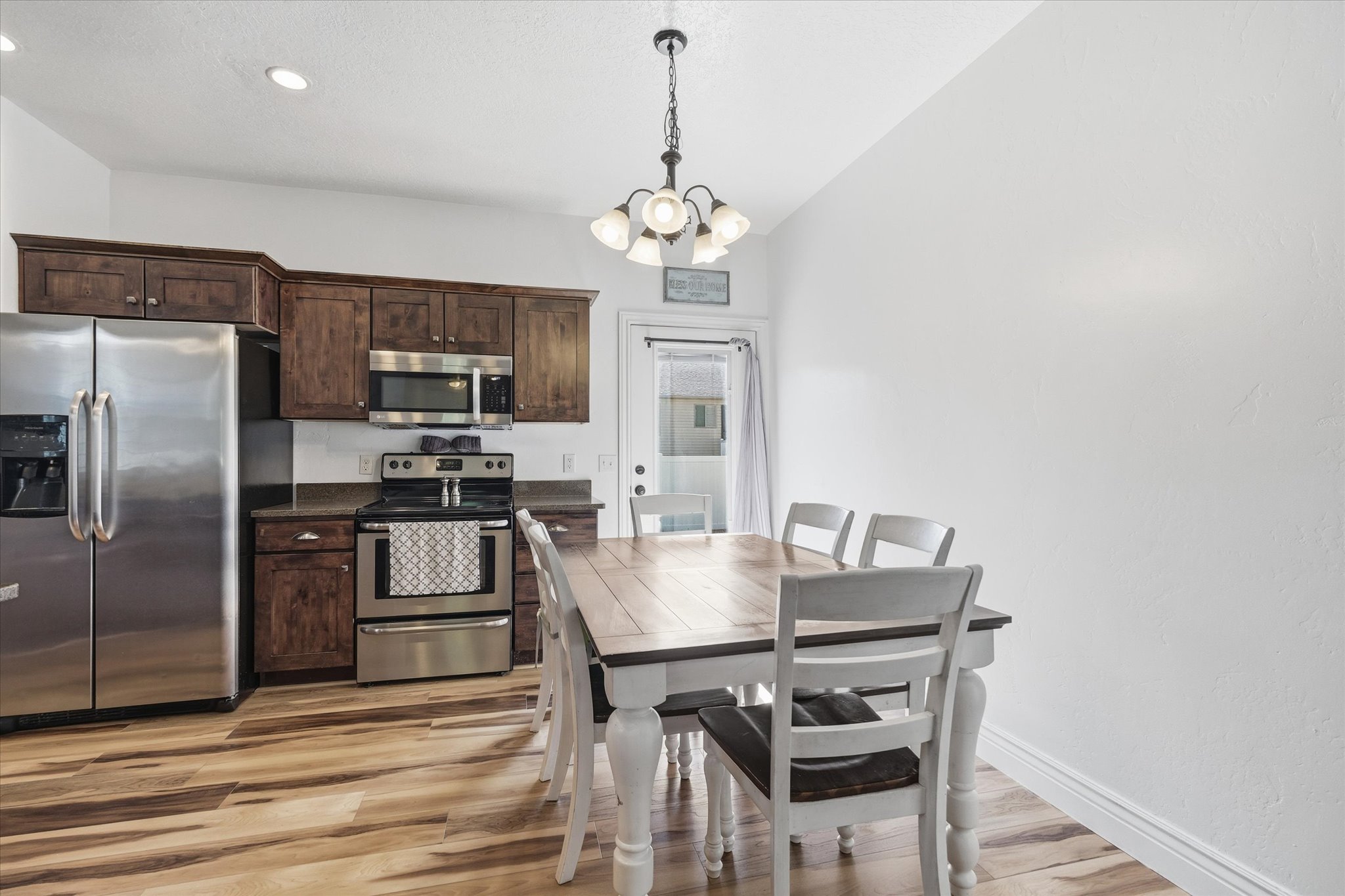 Kitchen and dining area featuring wood-finish flooring, dark wood cabinetry, stainless steel appliances, and recessed lighting