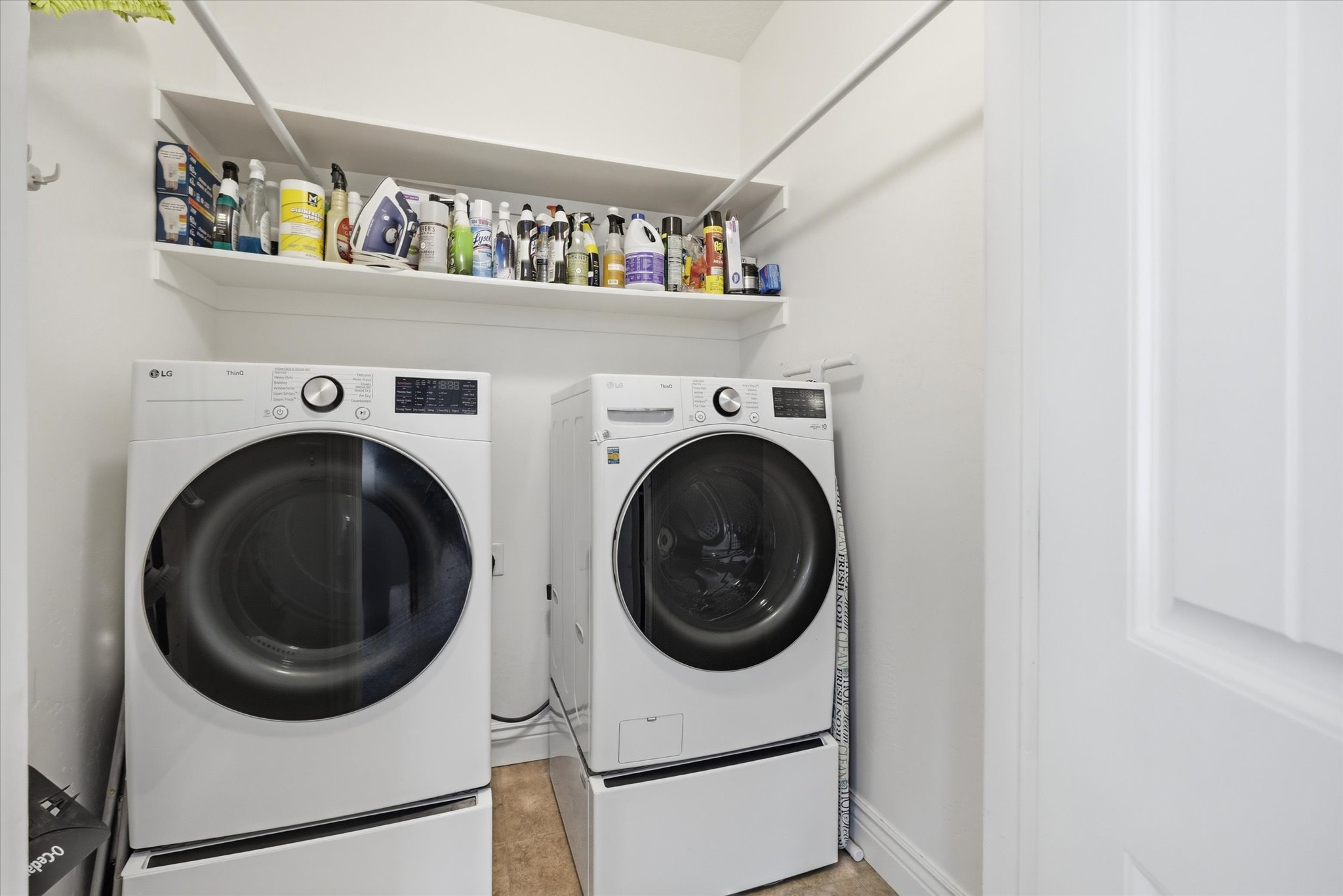 Dedicated laundry area featuring a white floating shelf, white walls, and light-toned flooring