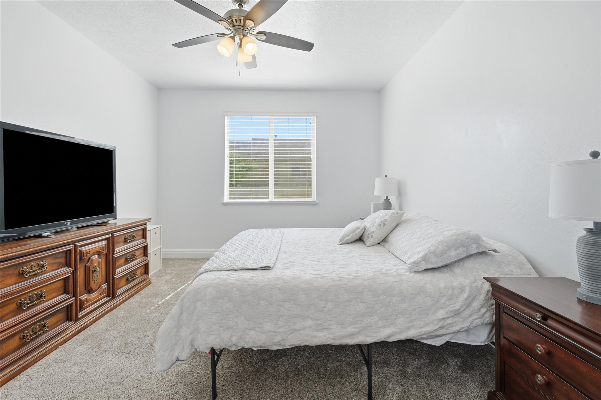 Carpeted interior with light-colored walls, a window featuring blinds, and a ceiling fan with integrated lighting
