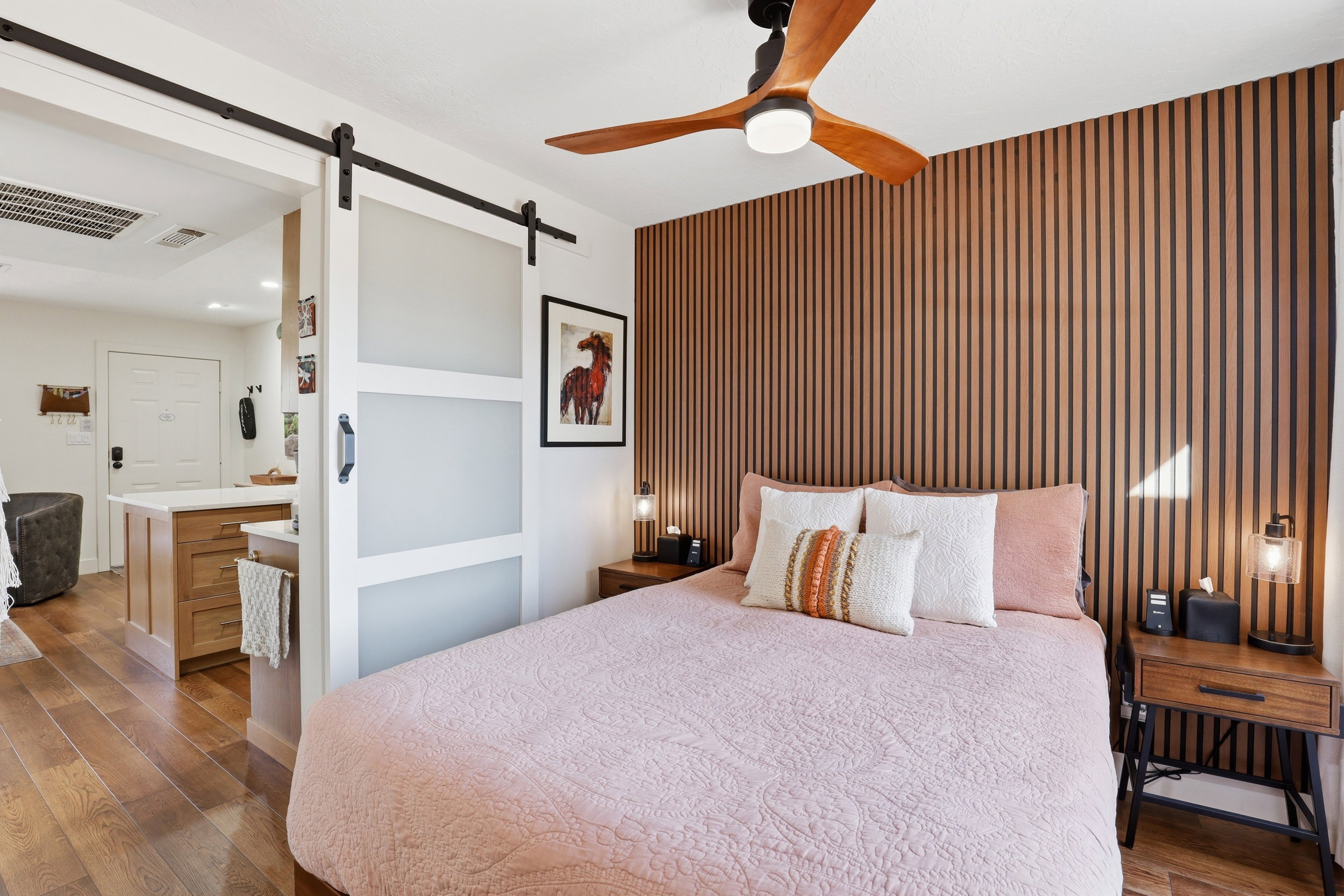 Bedroom featuring a slat wall accent, wood-finish flooring, and a modern ceiling fan