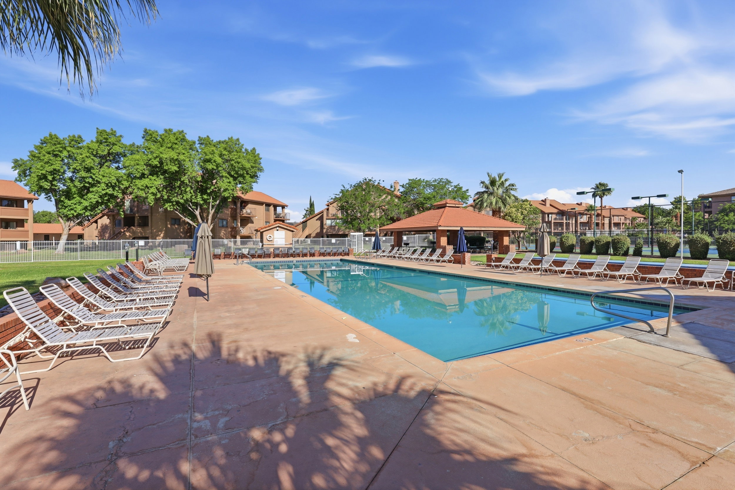 Expansive swimming pool with surrounding concrete decking, featuring a shaded cabana structure and multiple lounge chairs