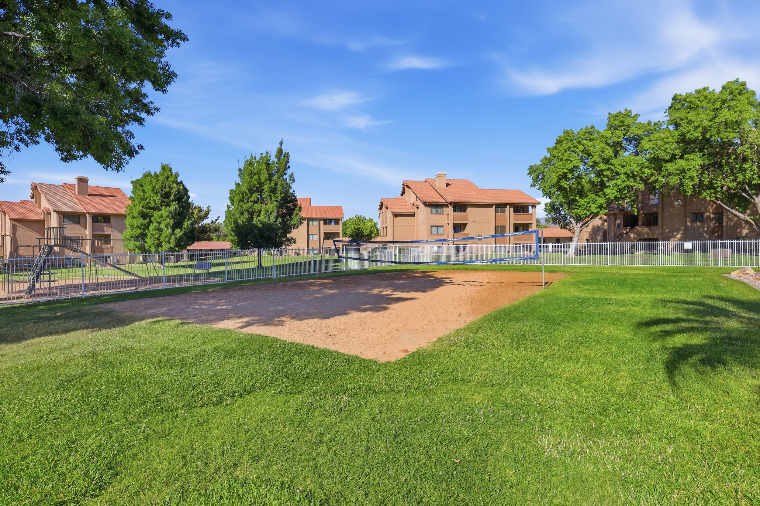 Outdoor sand court surrounded by turf lawn and mature trees