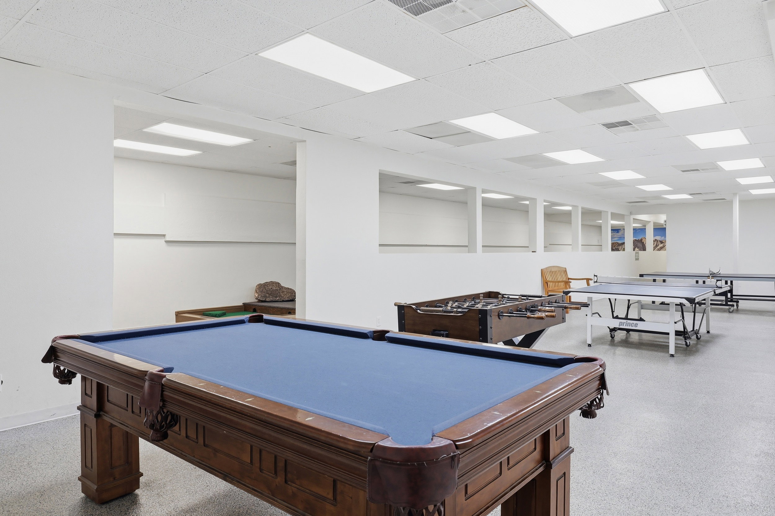 Recreation room featuring a pool table with ornate wooden legs and a blue felt surface, along with a foosball table and multiple ping pong tables