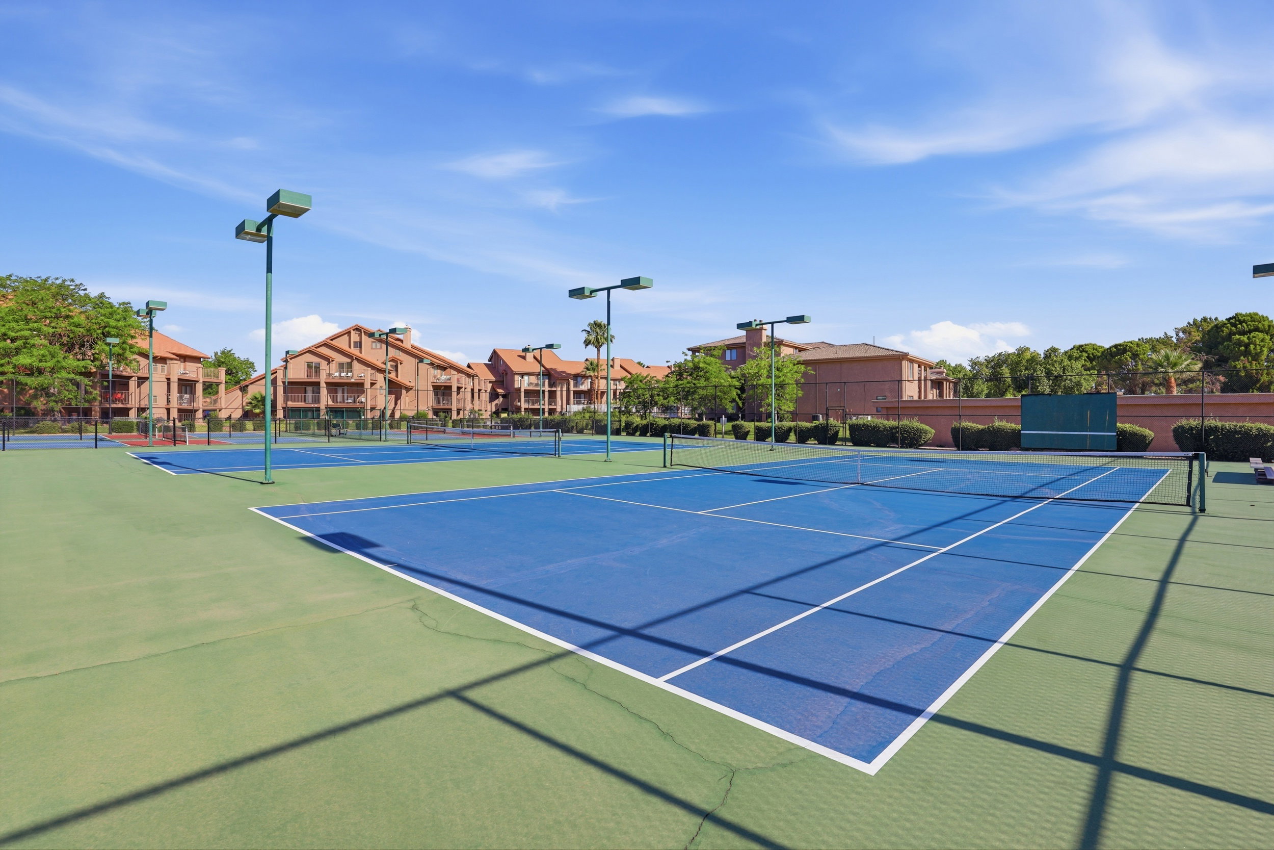 Multiple tennis courts with blue playing surfaces and green surrounds