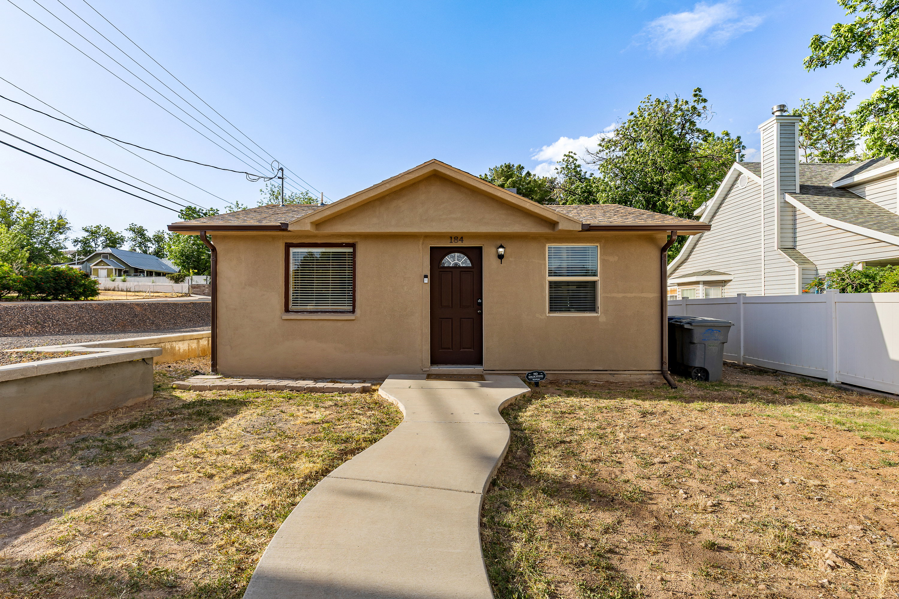 Stucco exterior featuring a dark brown front door with an arched window, a curved concrete walkway, and a white privacy fence